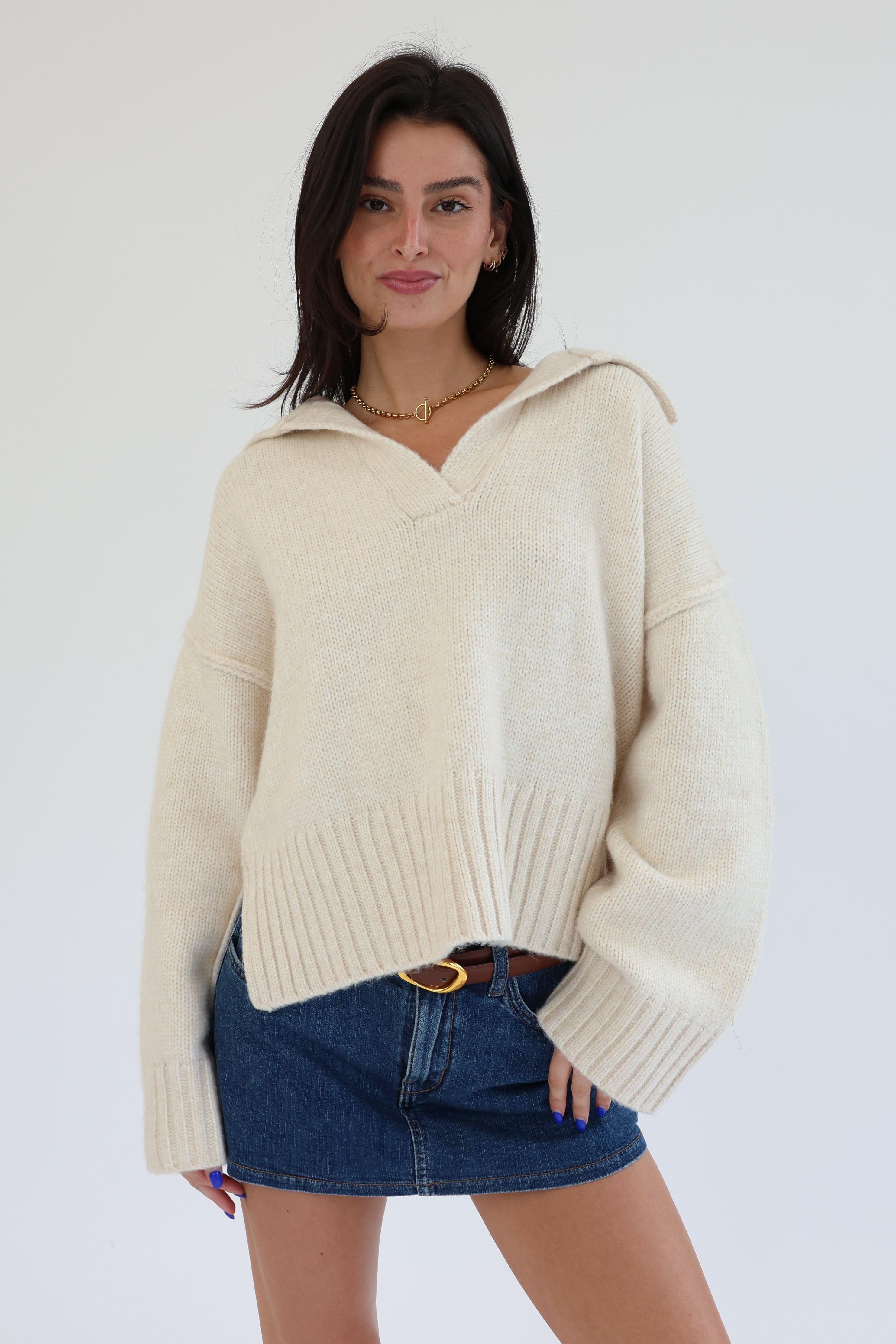 Woman wearing a cream sweater with a hood and denim shorts on a white background