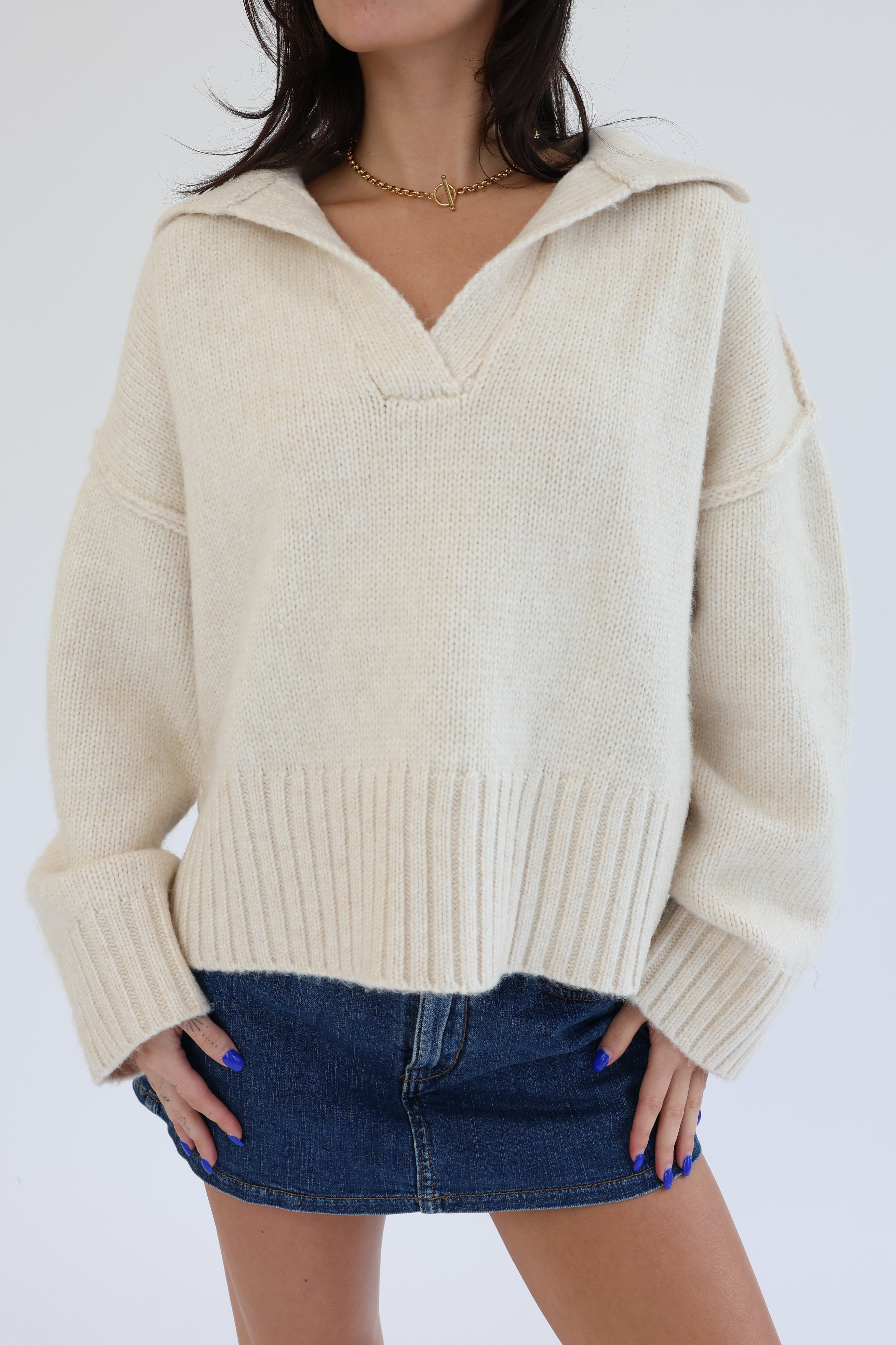 Person wearing a beige sweater with a hood and a denim skirt on a white background