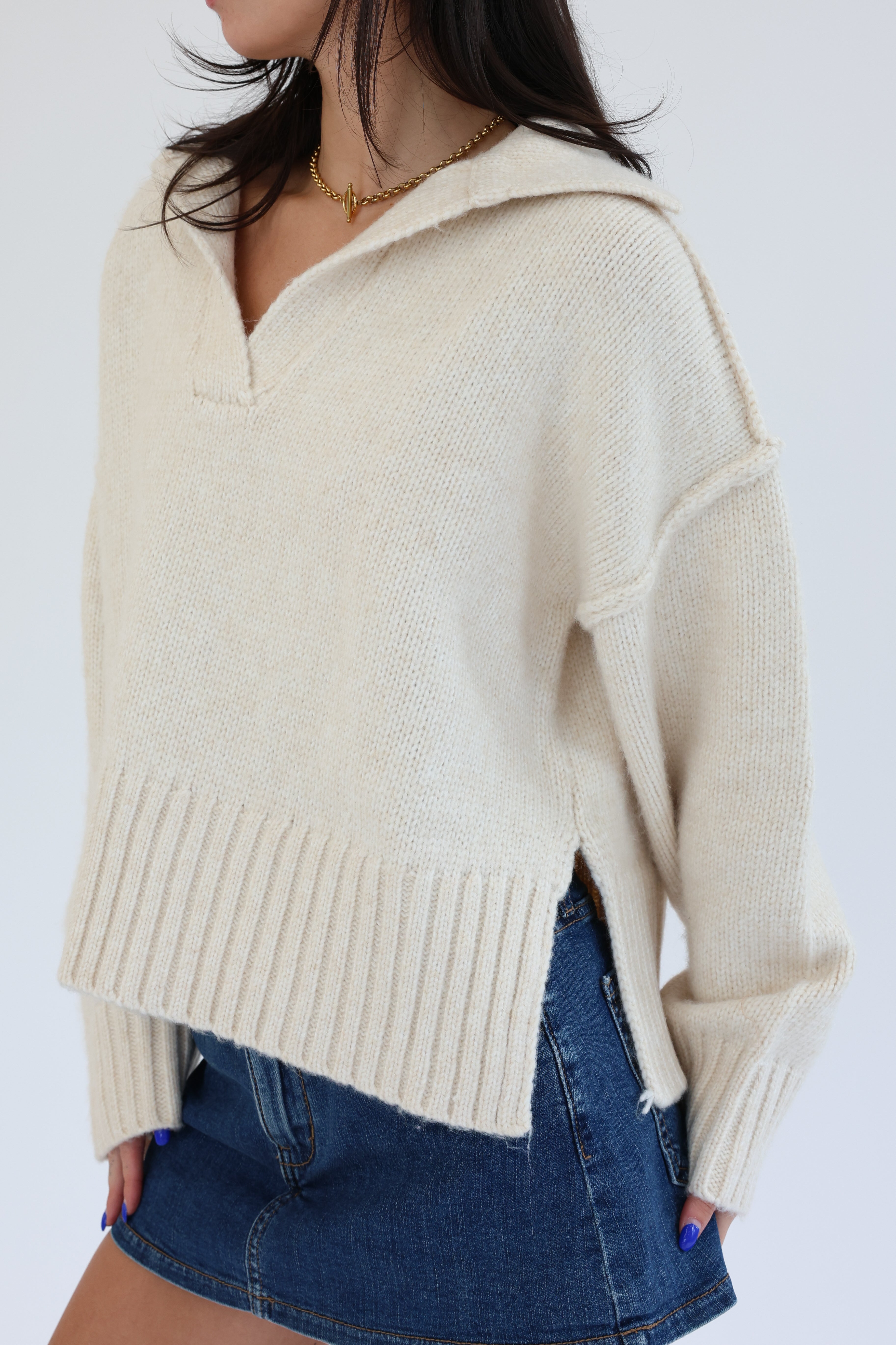 Person wearing a beige sweater and blue denim skirt on a white background