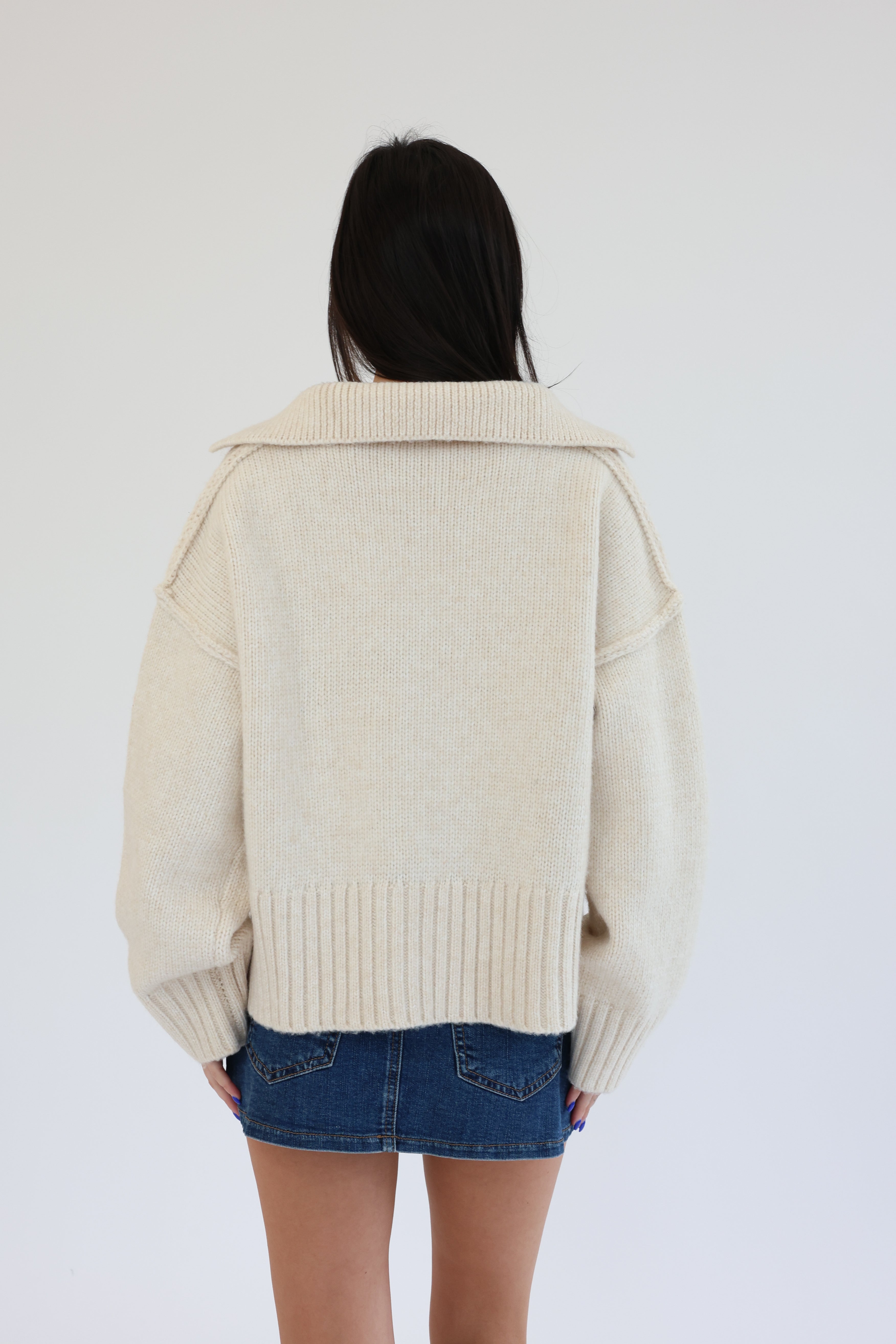 Person wearing a cream sweater and denim shorts on a white background