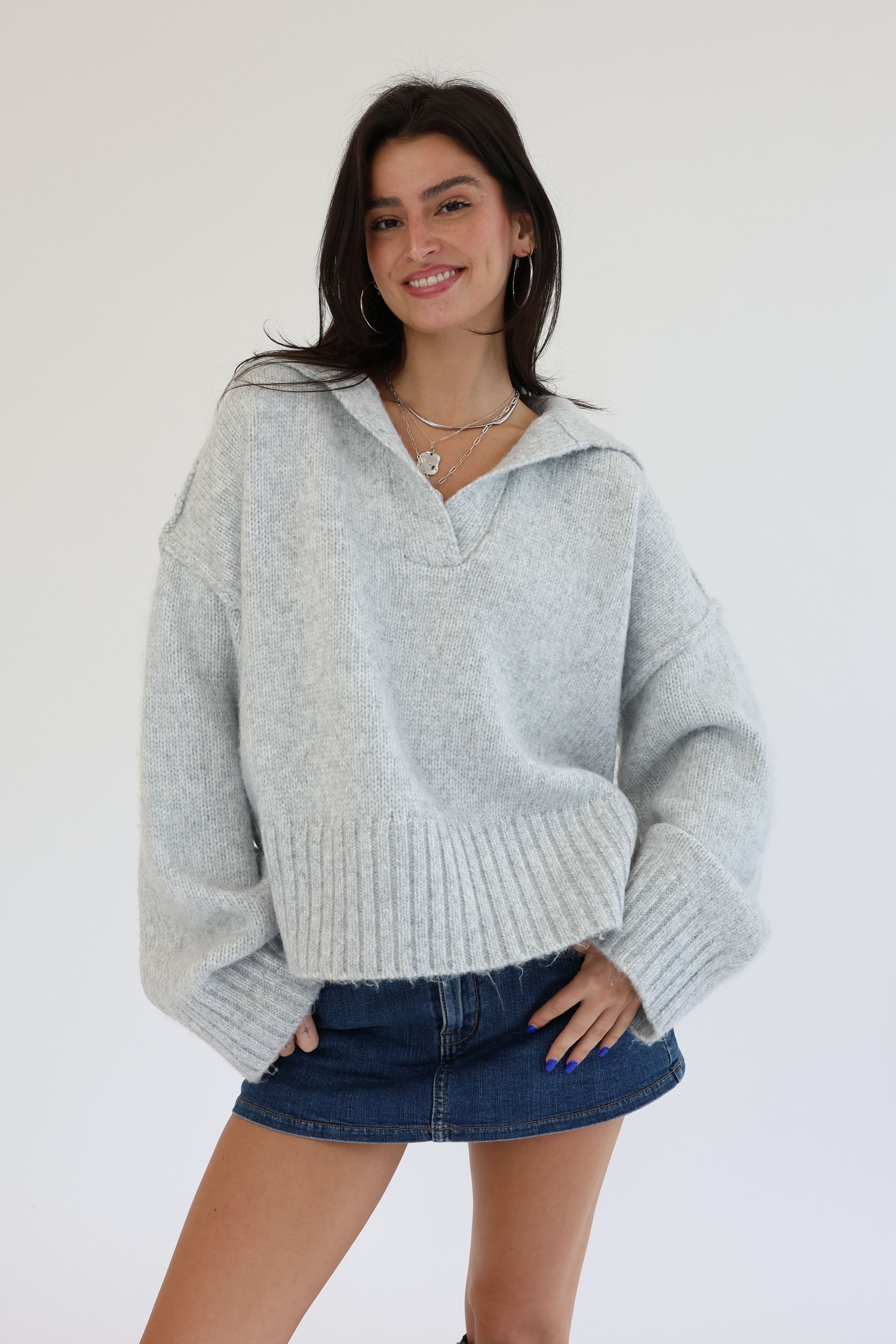 Woman wearing a light gray sweater and denim skirt on a white background