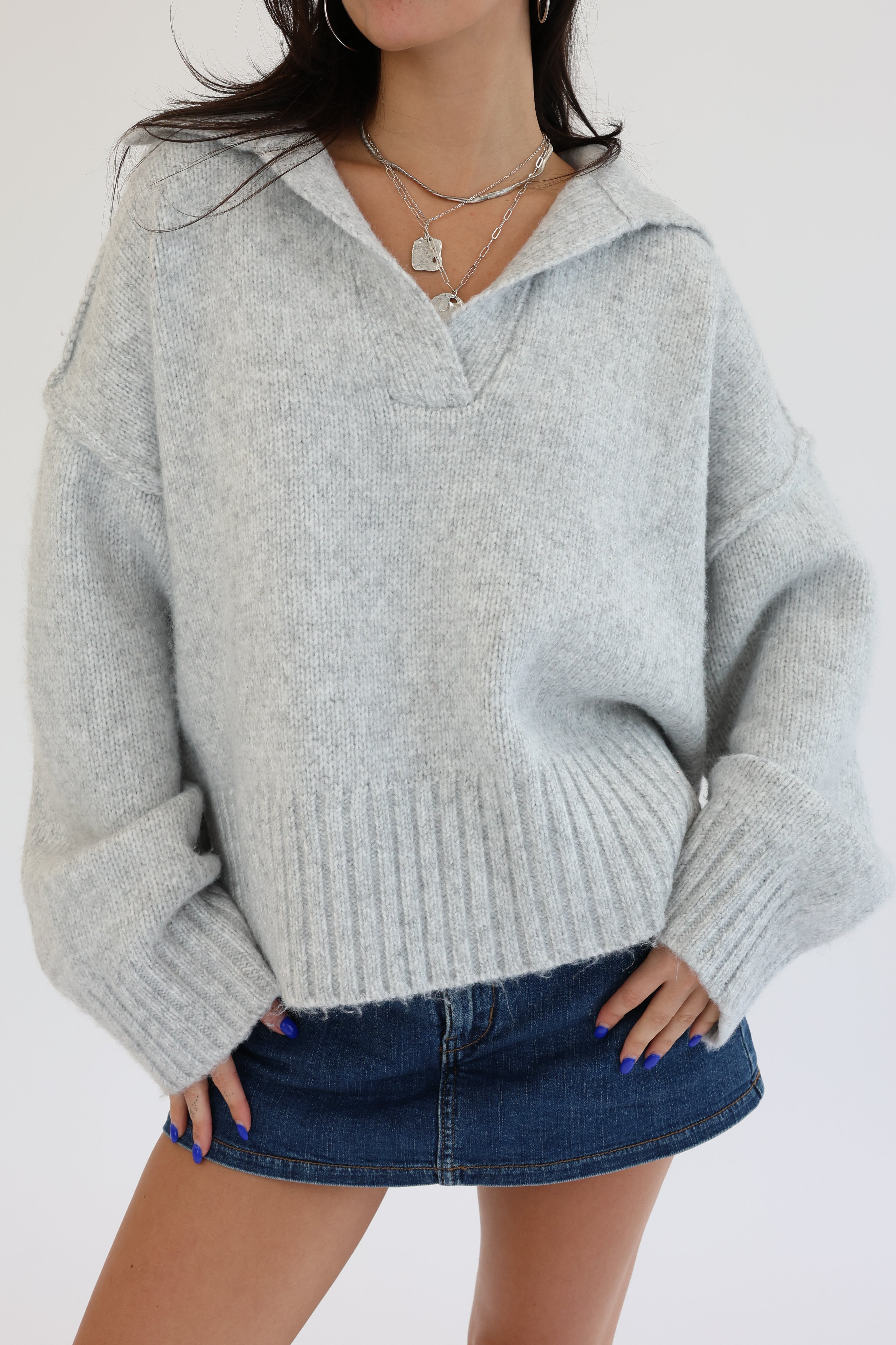 Person wearing a gray sweater and denim skirt on a white background
