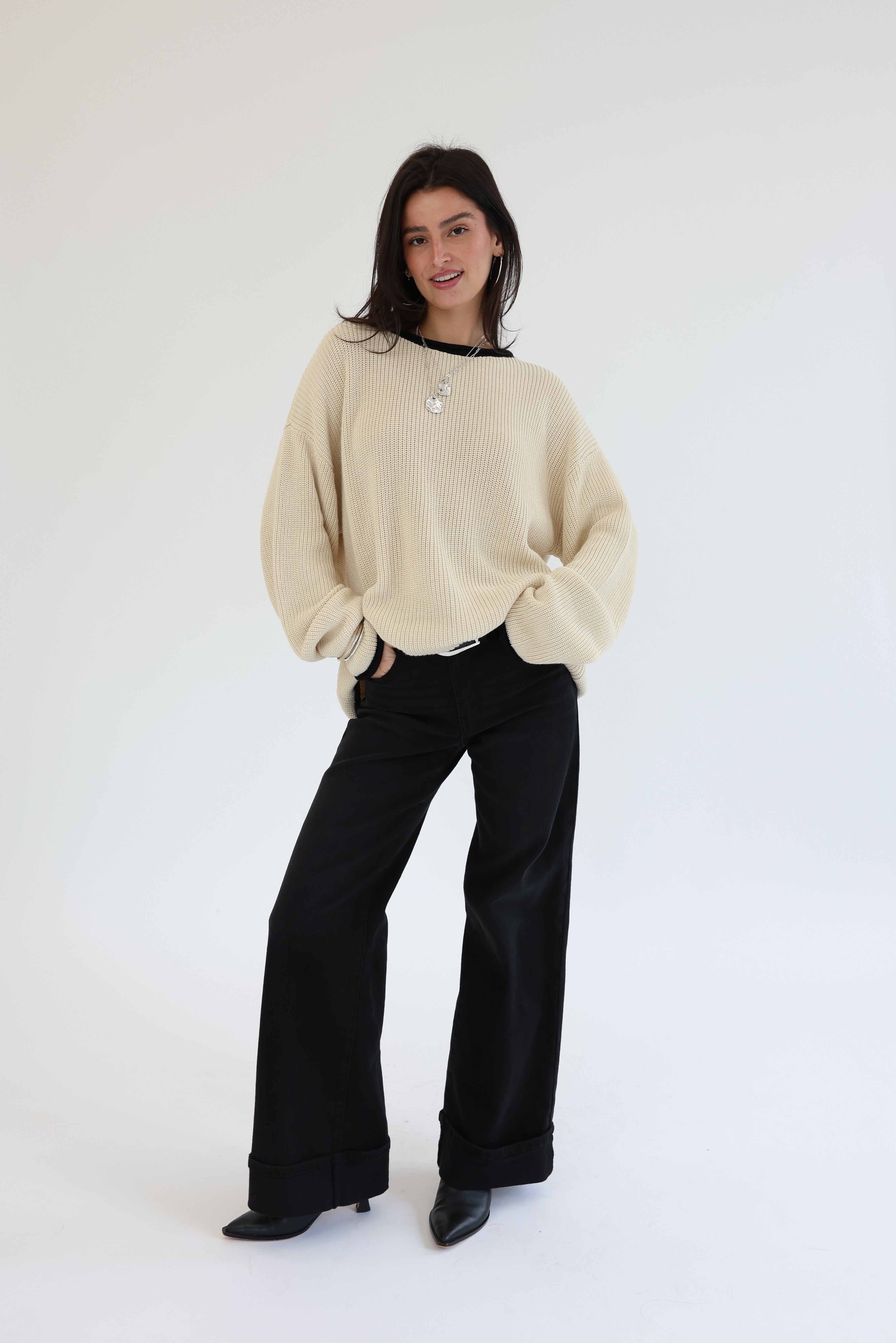 Person wearing a beige sweater and black pants on a white background