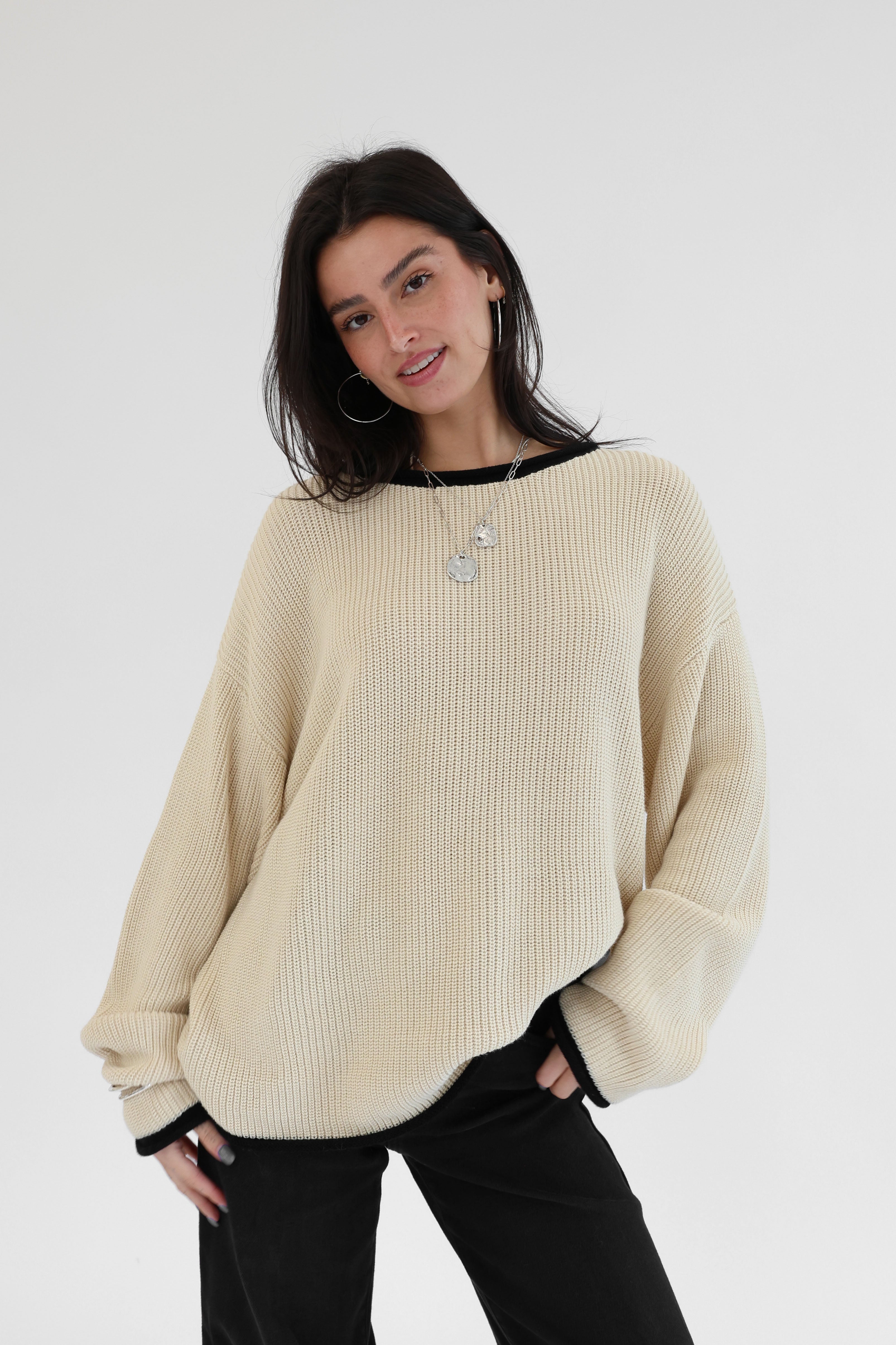 Woman wearing a beige sweater and black pants on a white background