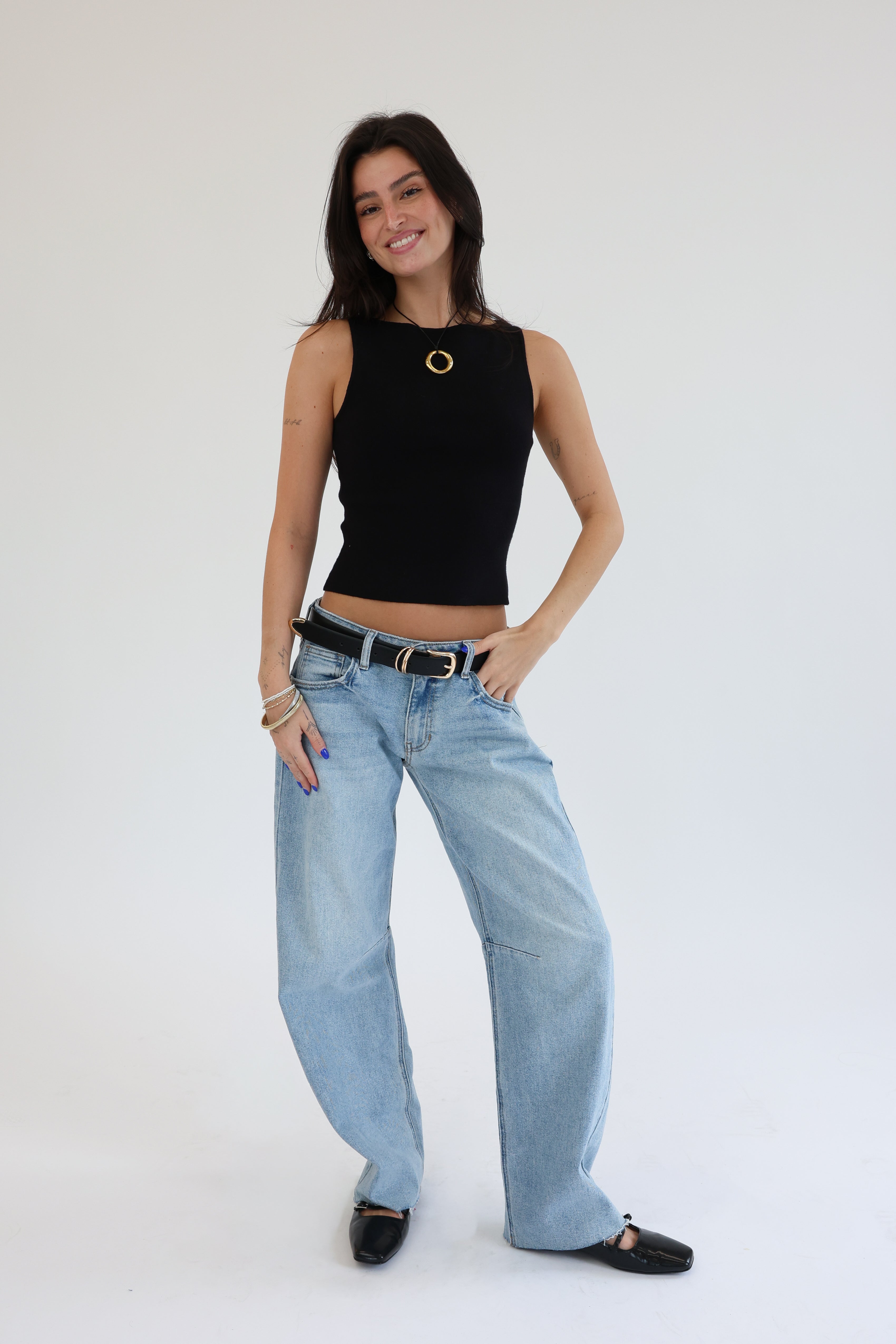 Woman wearing a black sleeveless top and light blue jeans on a white background