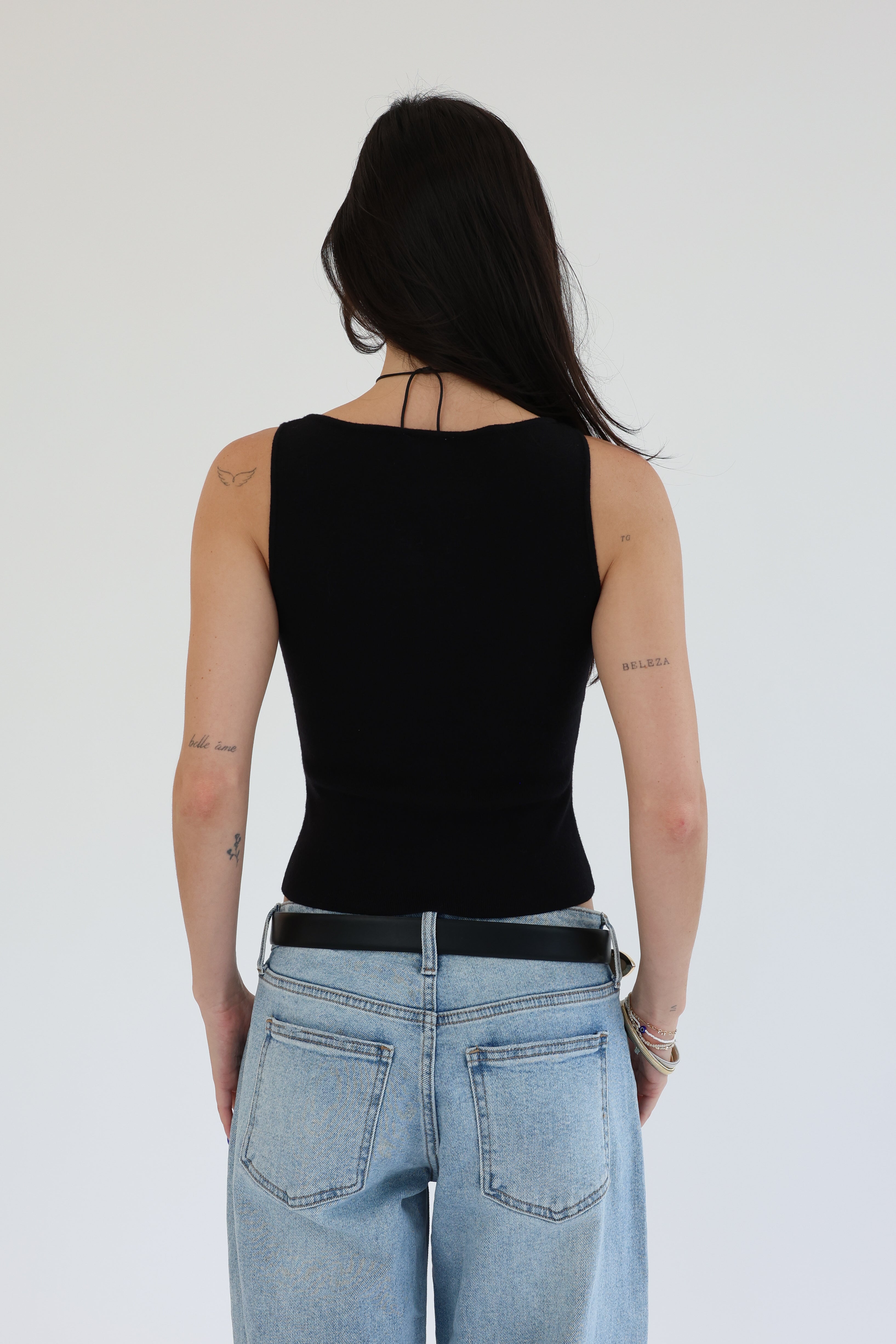 Person wearing a black tank top and blue jeans from behind on a white background