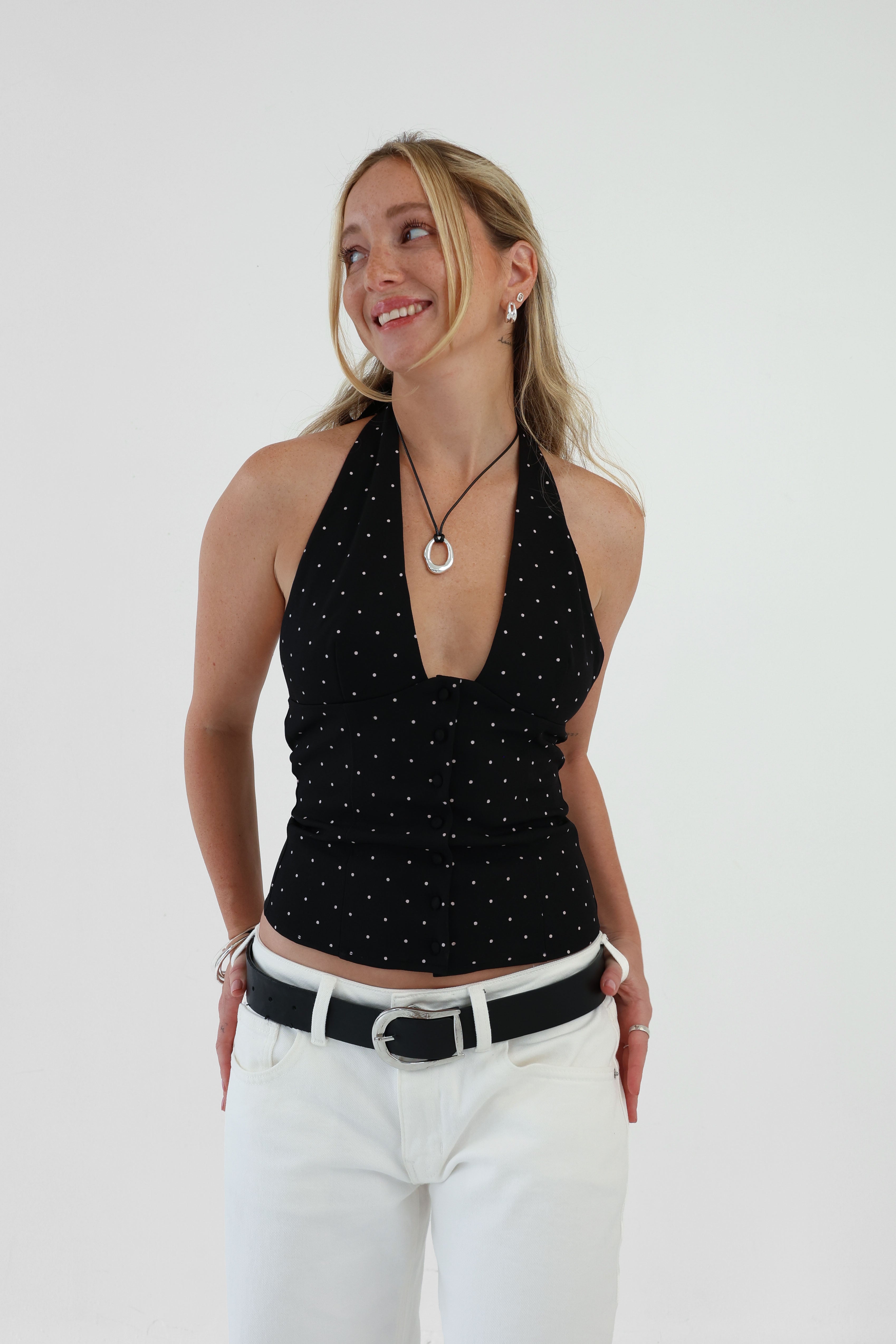 Woman wearing a black halter top with white polka dots and white pants against a plain background