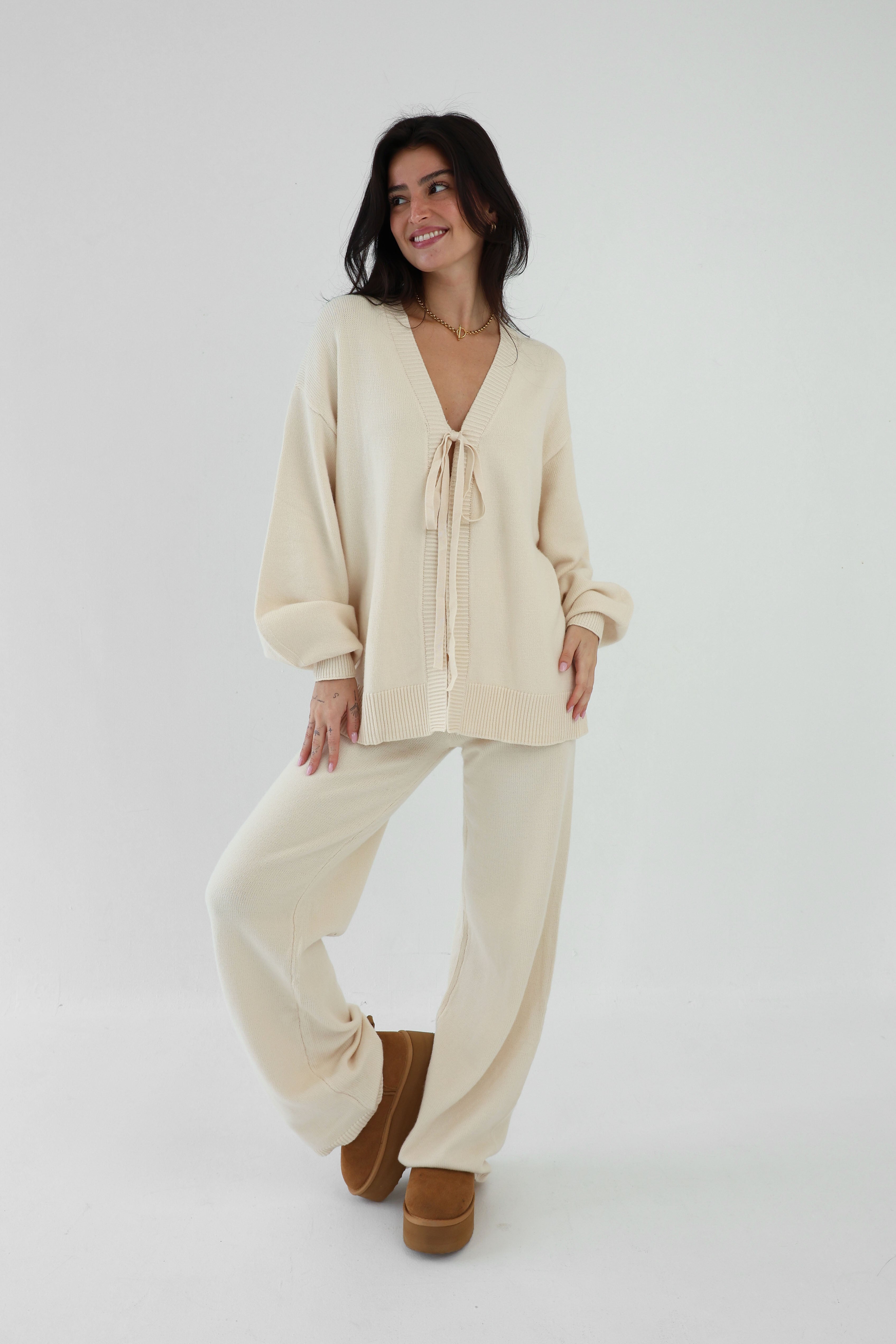 Woman wearing a beige outfit with a matching cardigan and pants on a white background