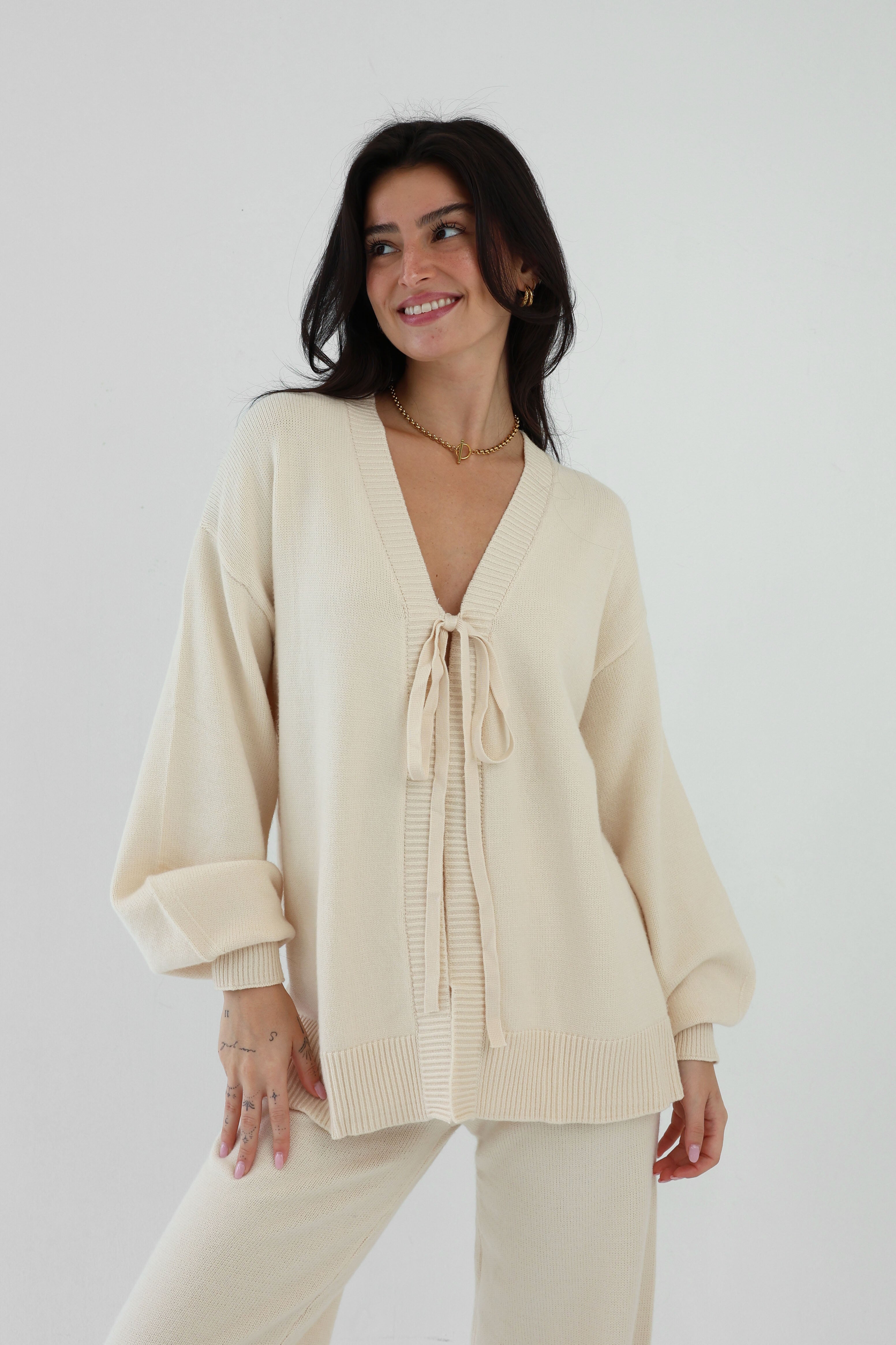 Woman wearing a beige cardigan and pants against a white background