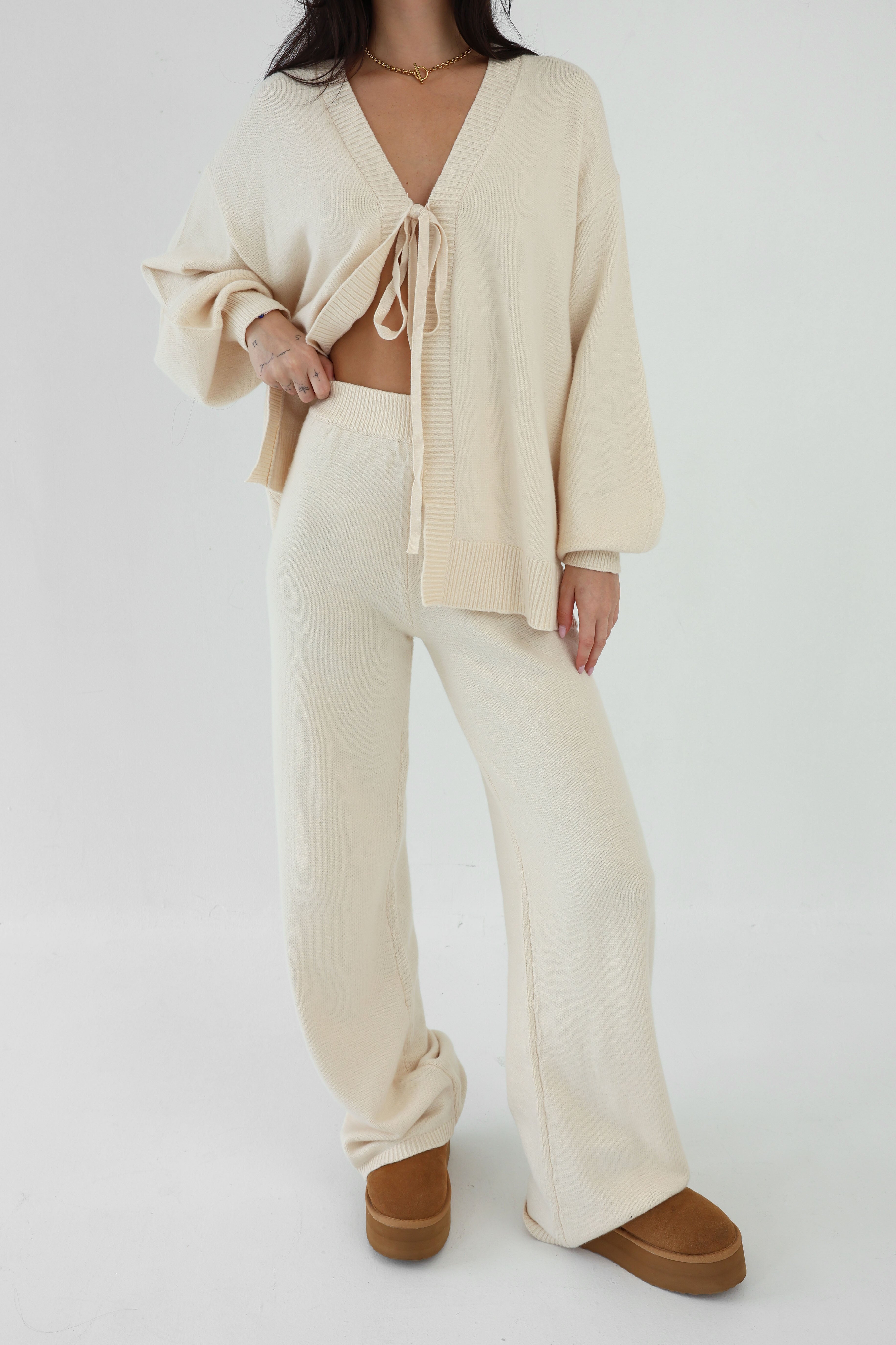 Person wearing a cream-colored outfit with wide-leg pants and brown shoes on a white background