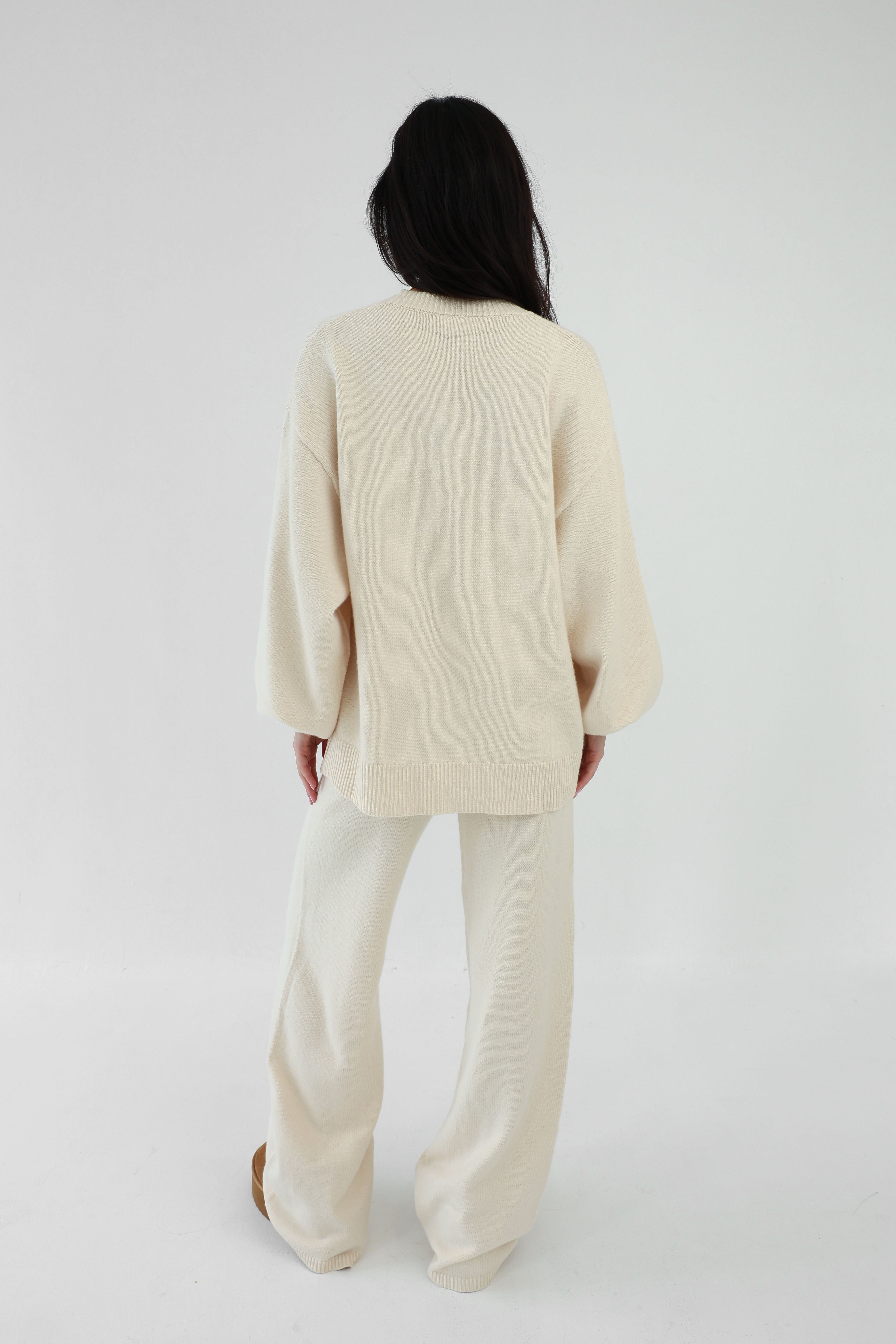 Person wearing a cream-colored cardigan and pants on a white background