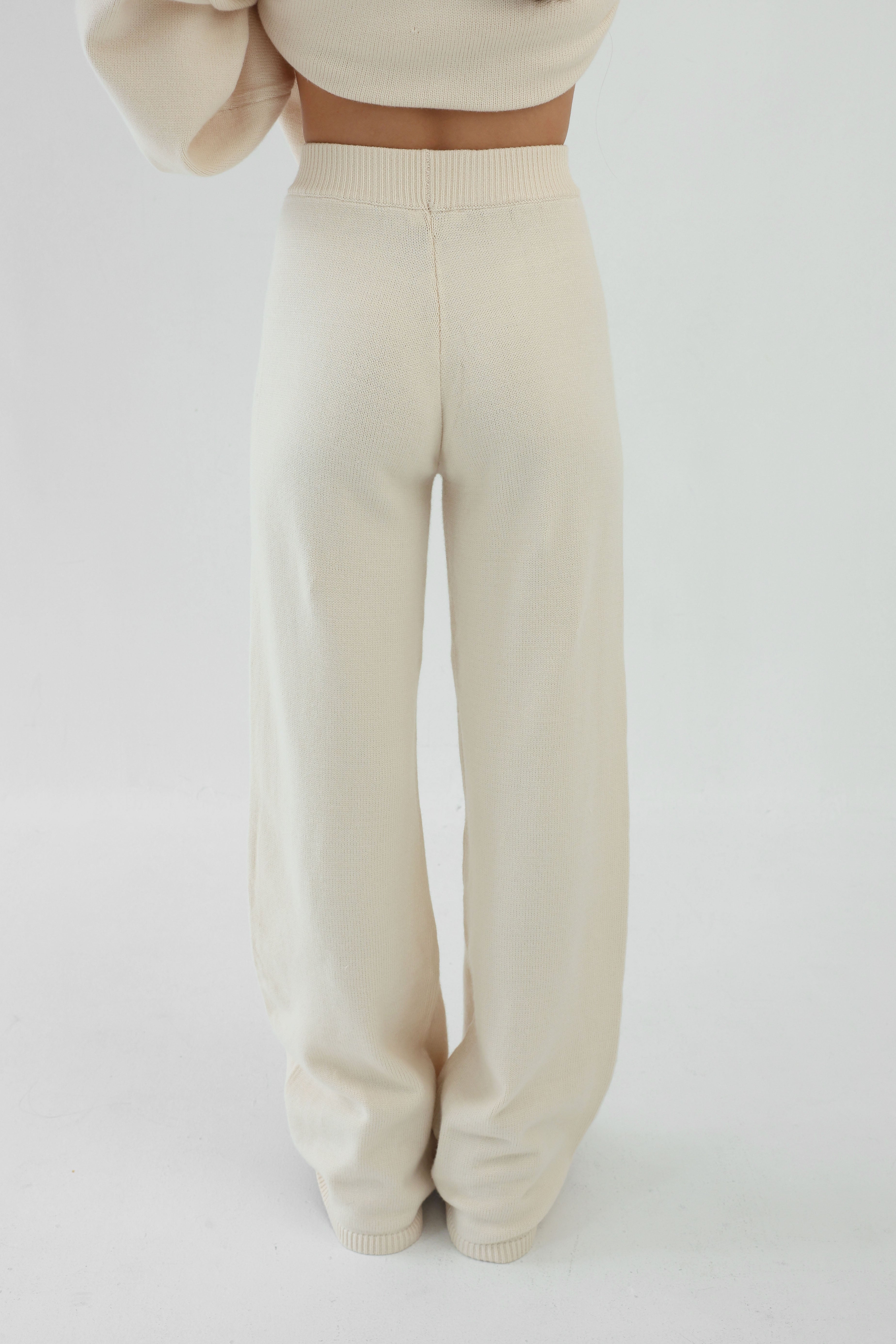 Beige knitted pants worn by a person on a white background