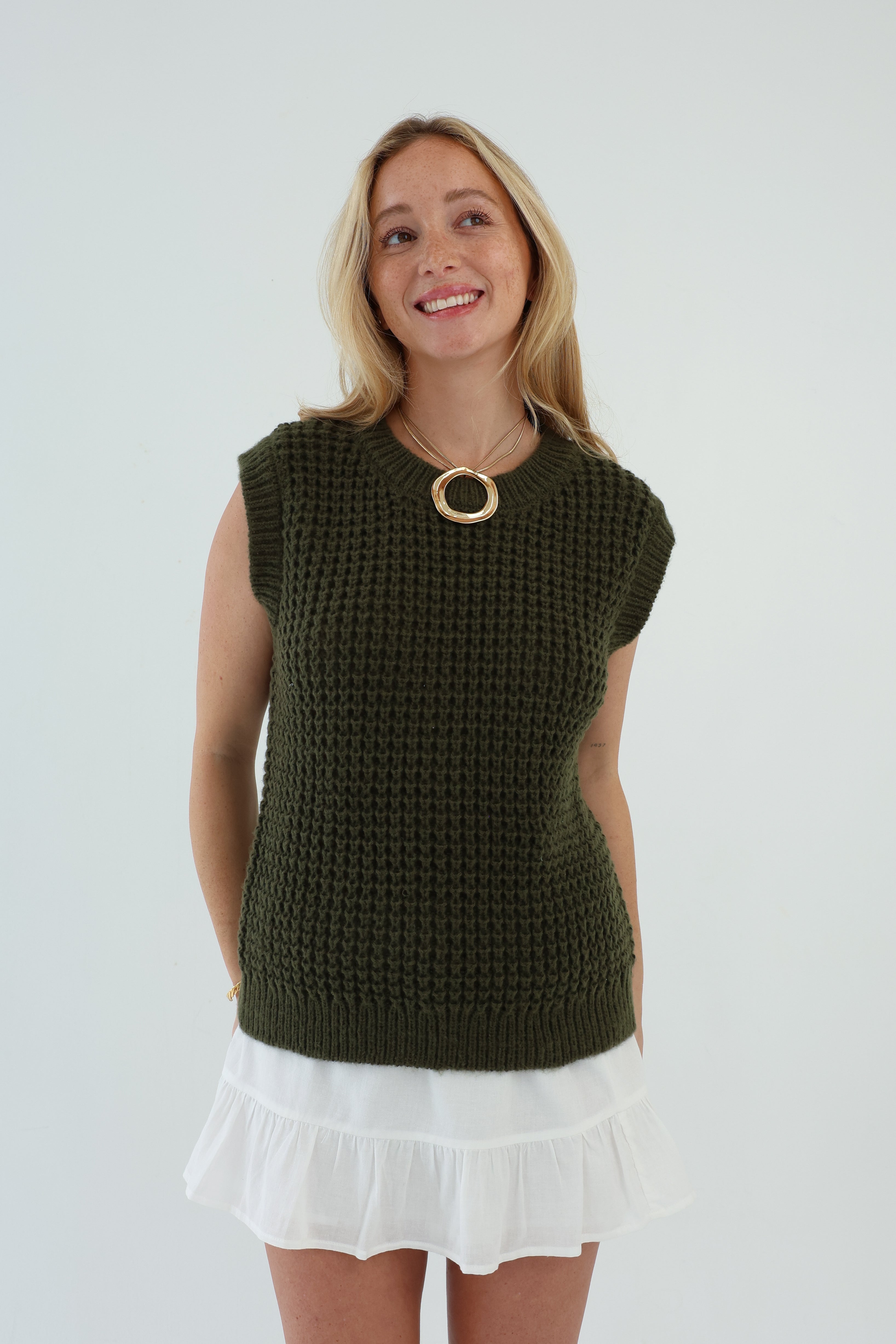 Woman wearing a green knitted sleeveless top and white skirt on a light gray background