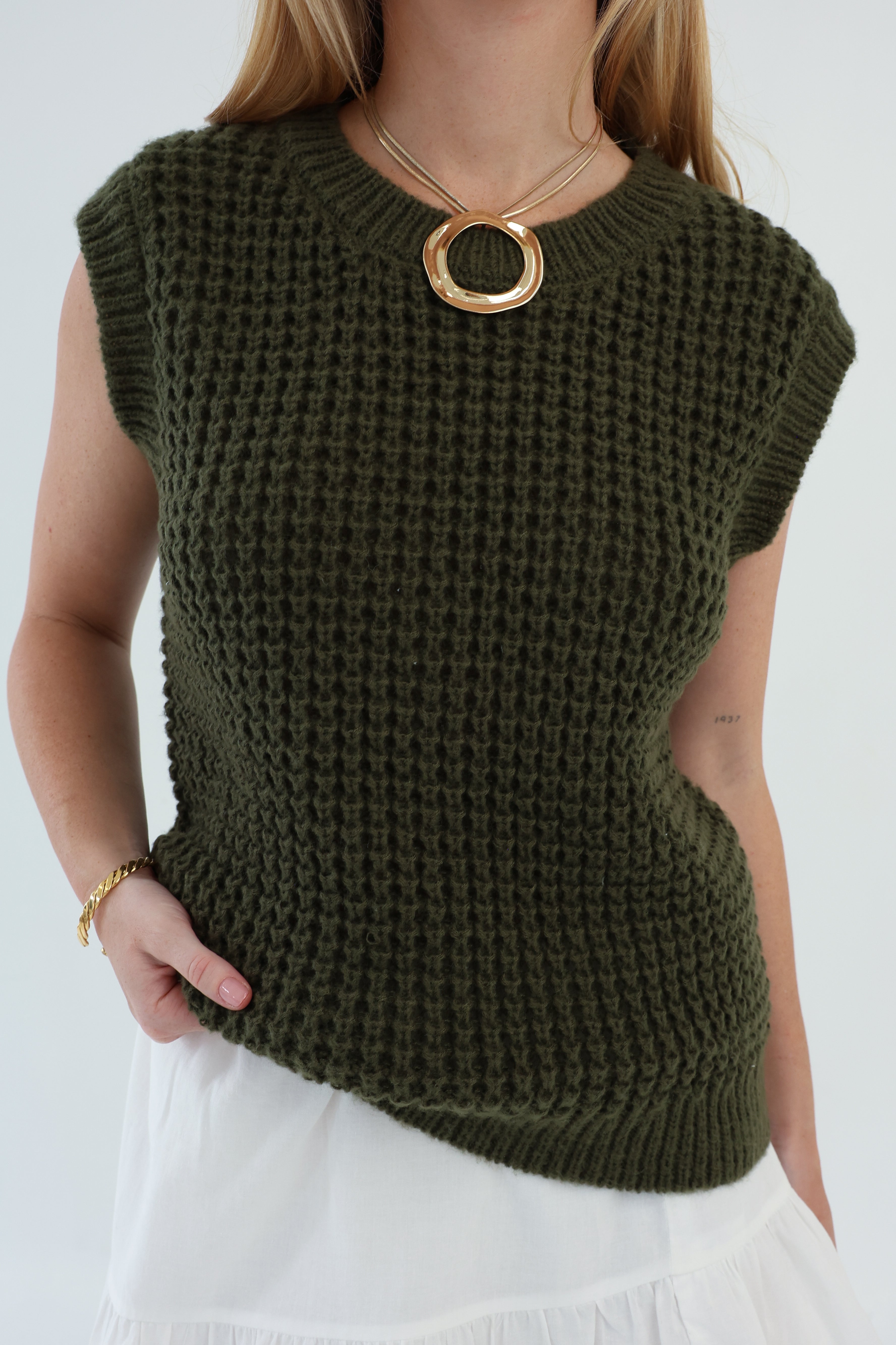 Person wearing a green knitted sleeveless top on a white background