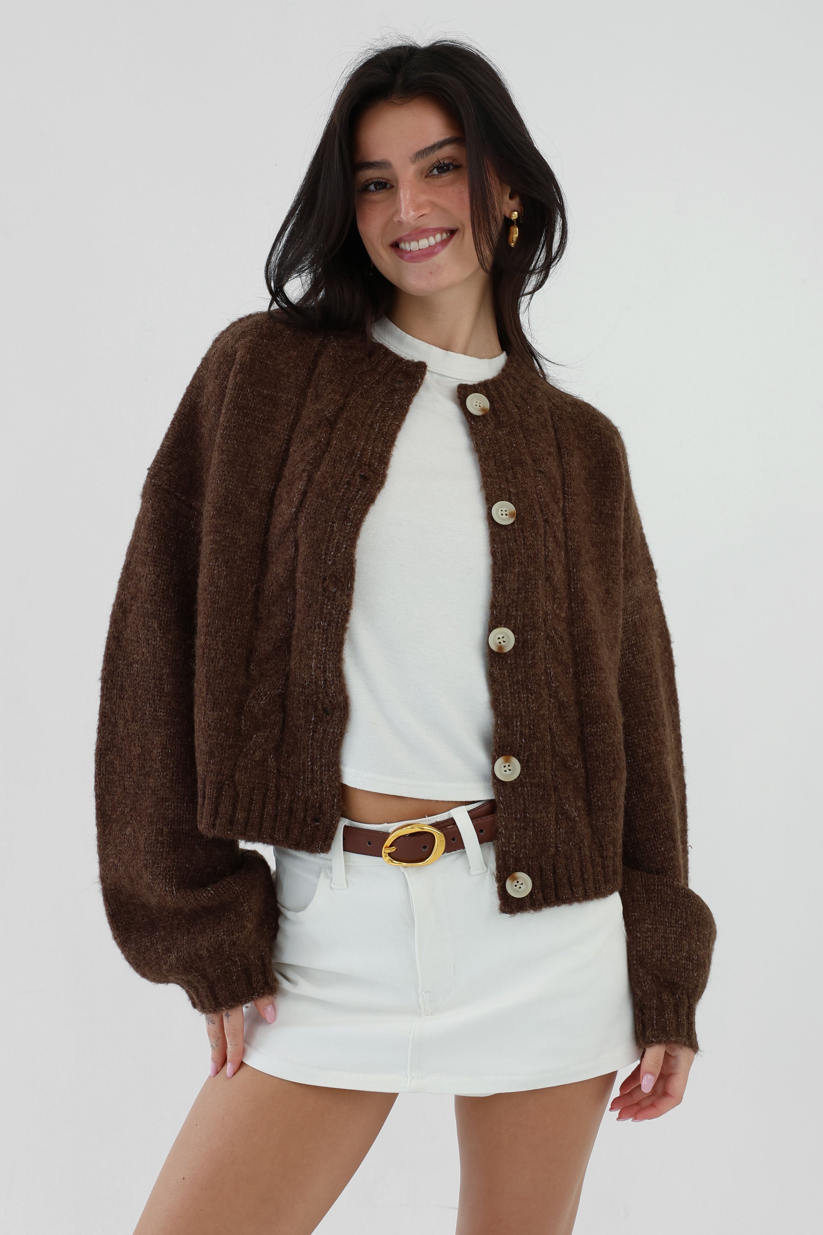 Woman wearing a brown cardigan over a white shirt and shorts on a white background
