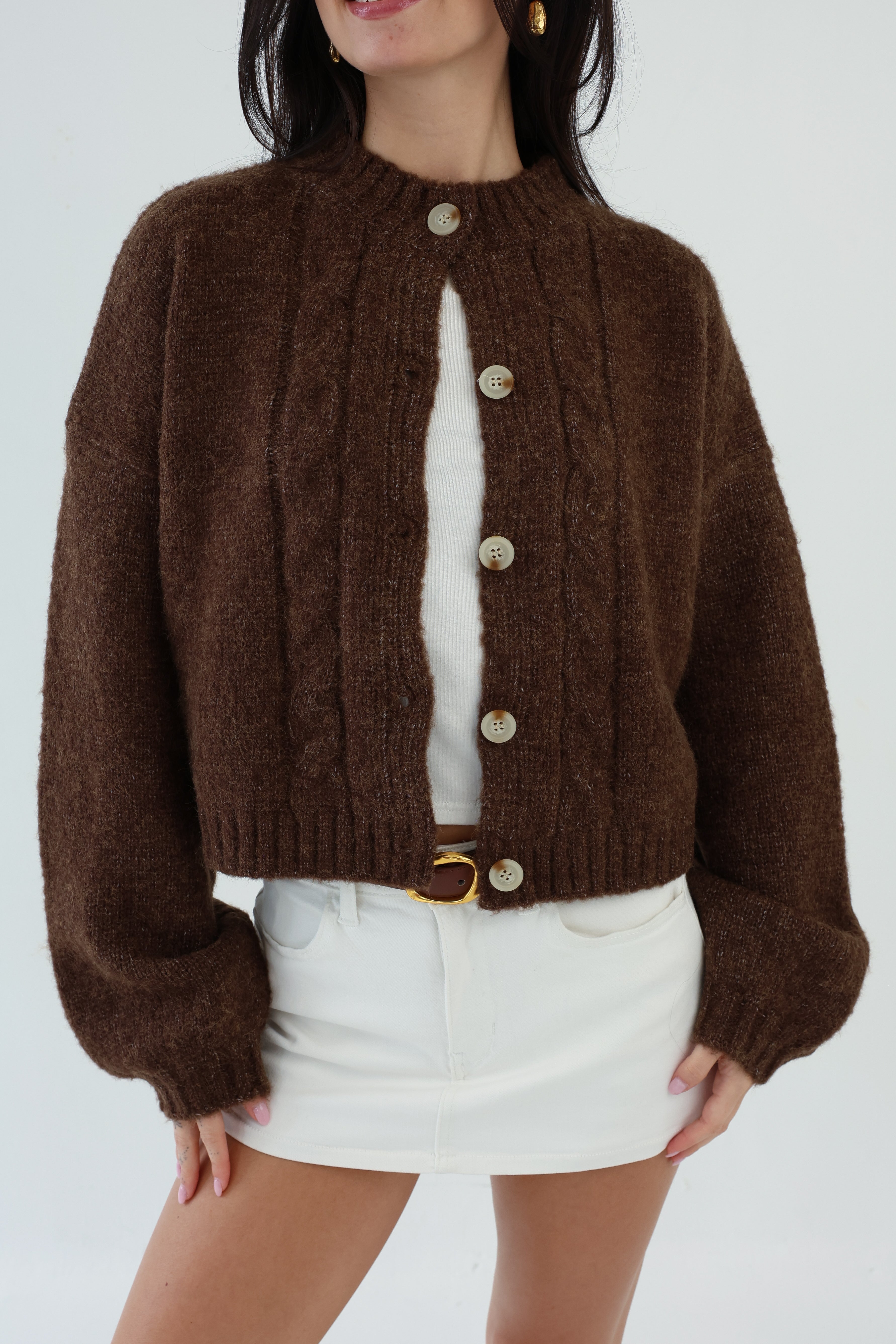 Person wearing a brown cardigan with buttons on a white background