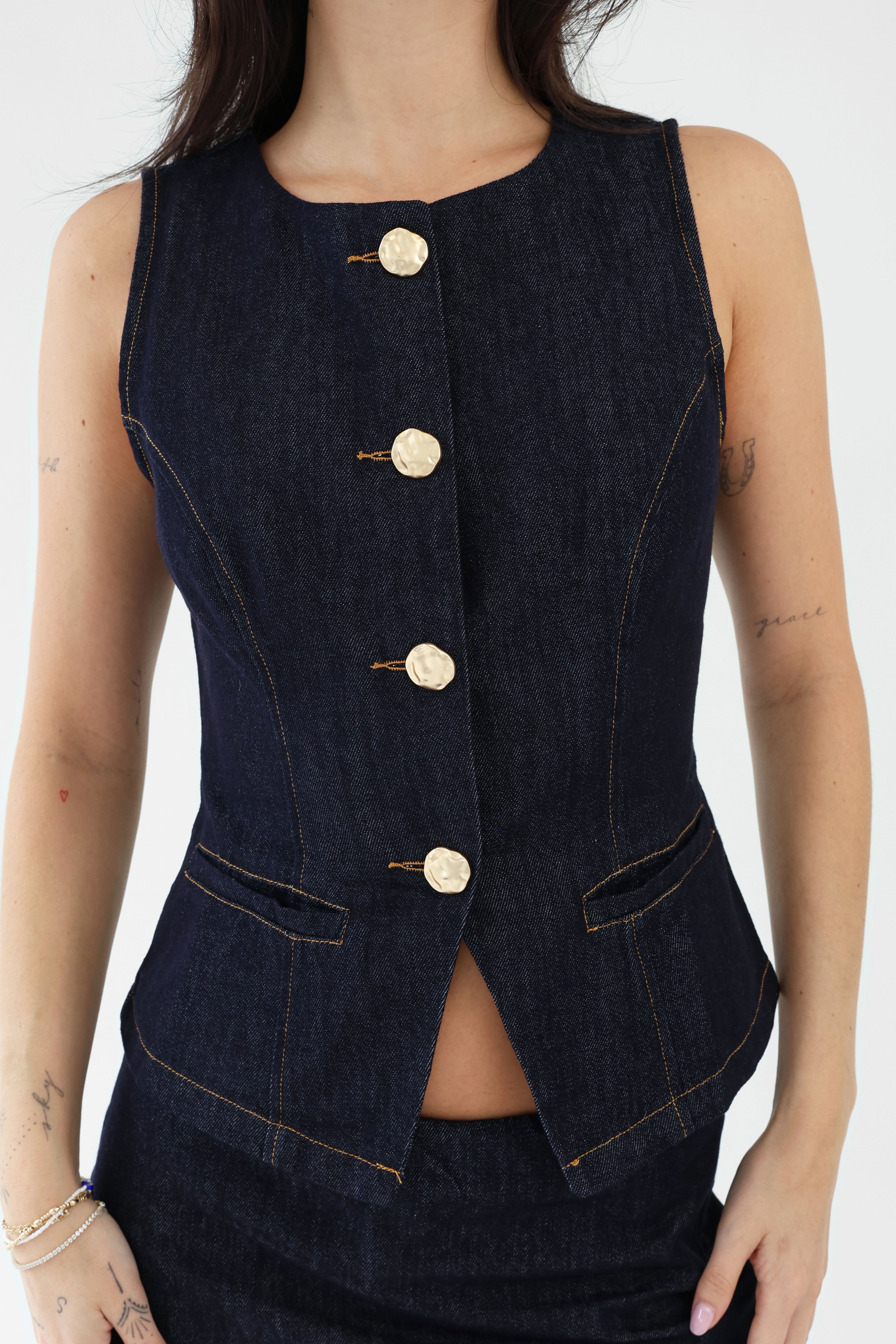 Dark denim vest with gold buttons worn by a person on a white background