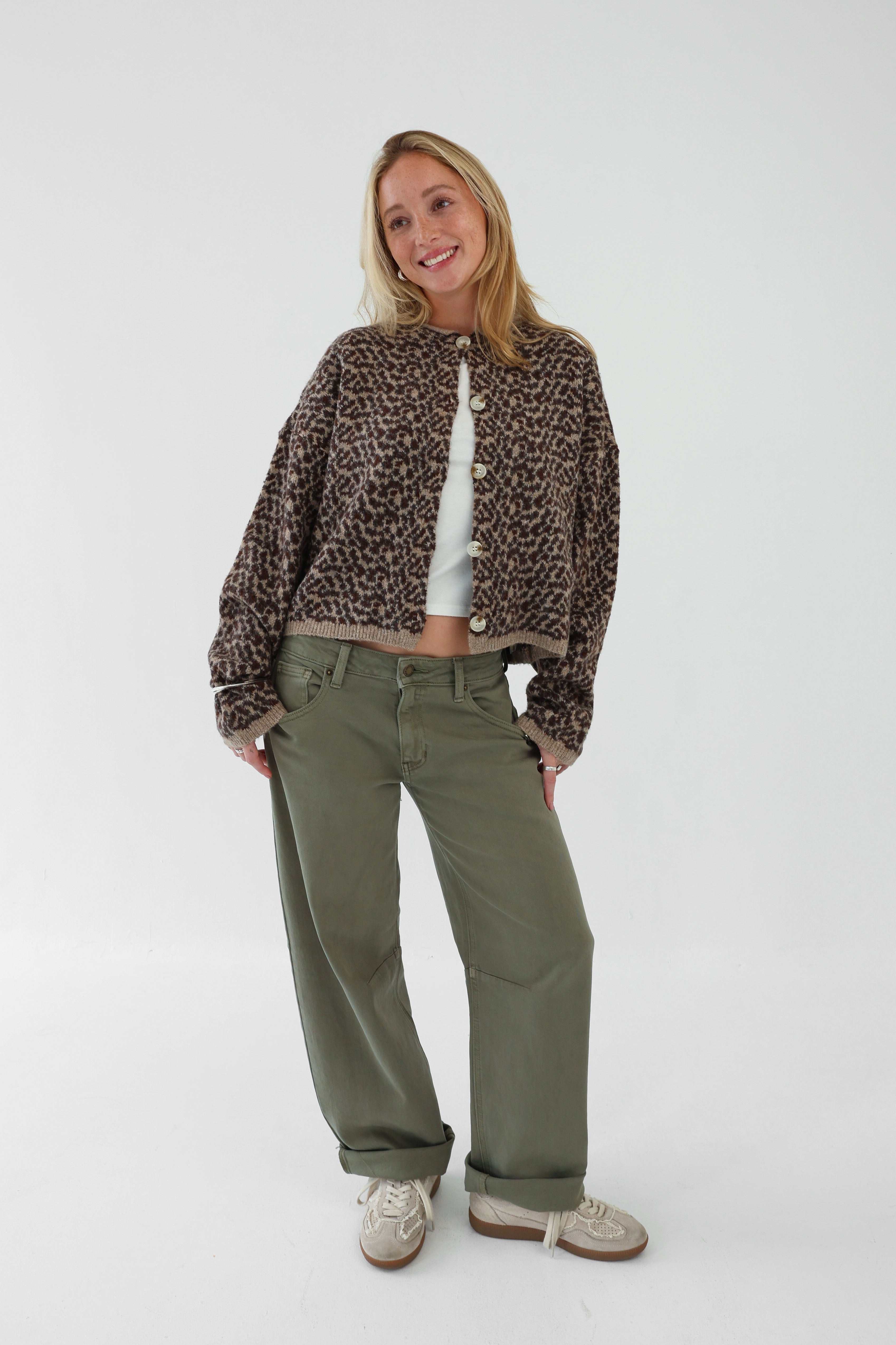 Woman wearing a leopard print jacket and green pants on a white background