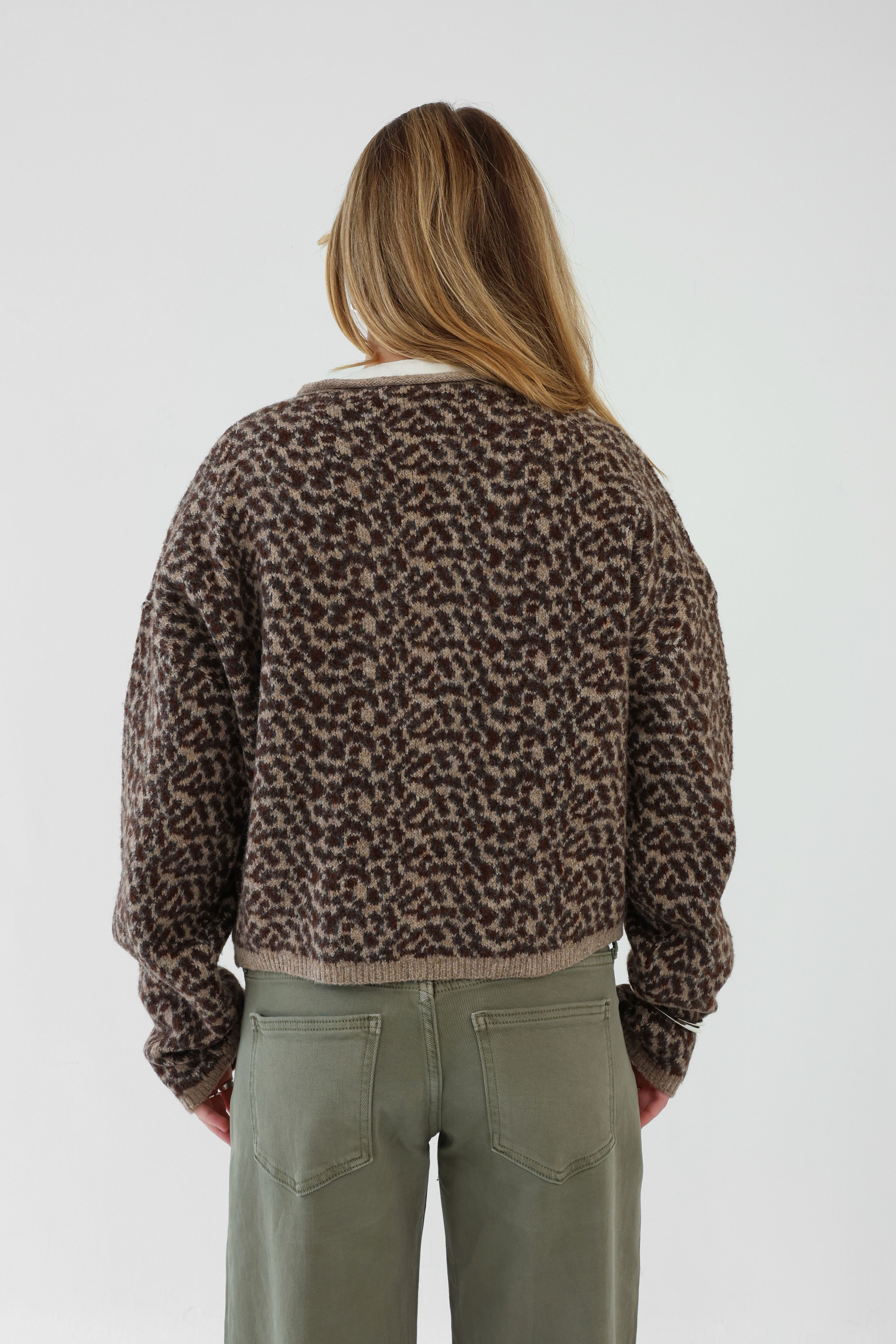 Person wearing a leopard print sweater and green pants on a white background