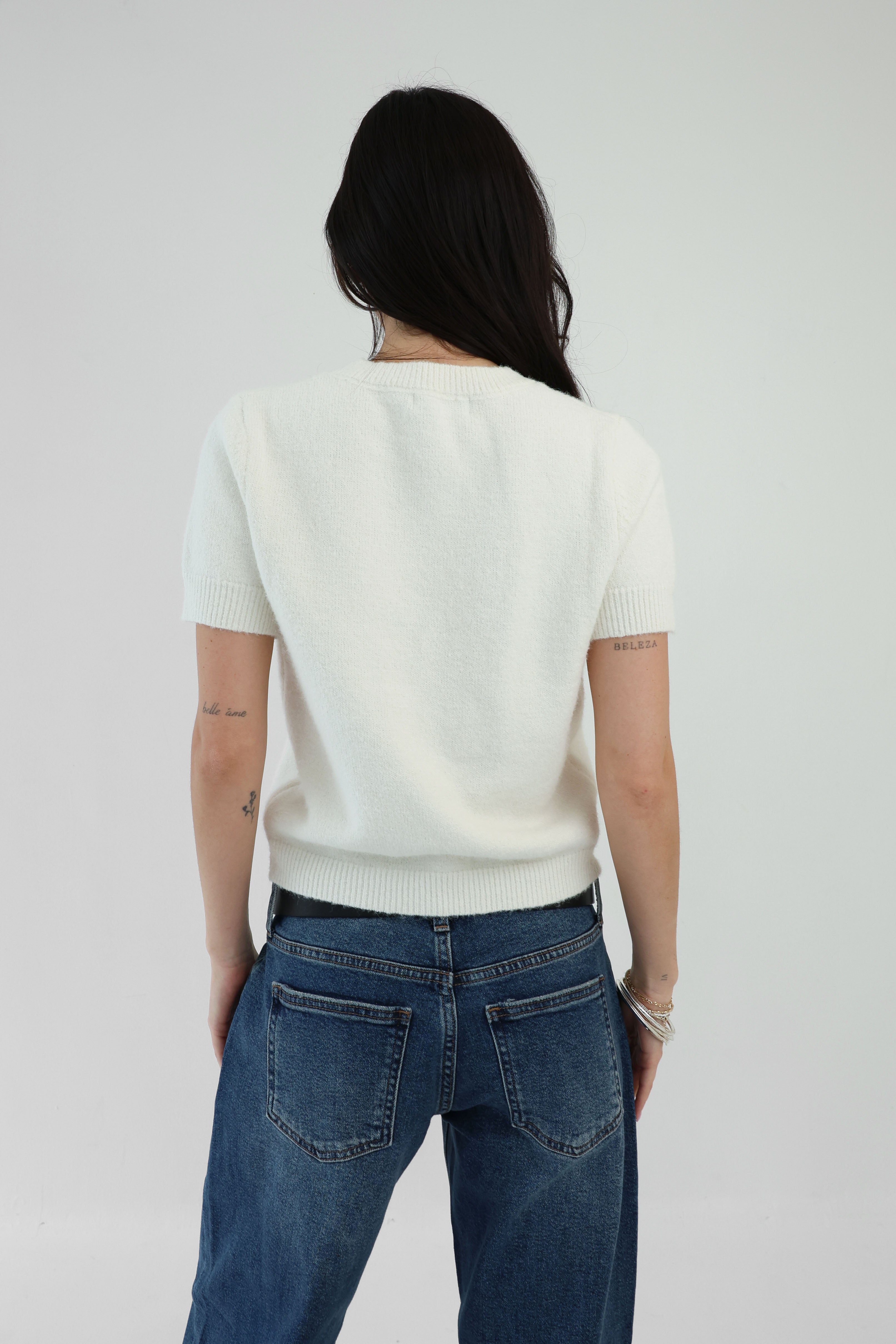 Person wearing a white sweater and blue jeans against a plain background