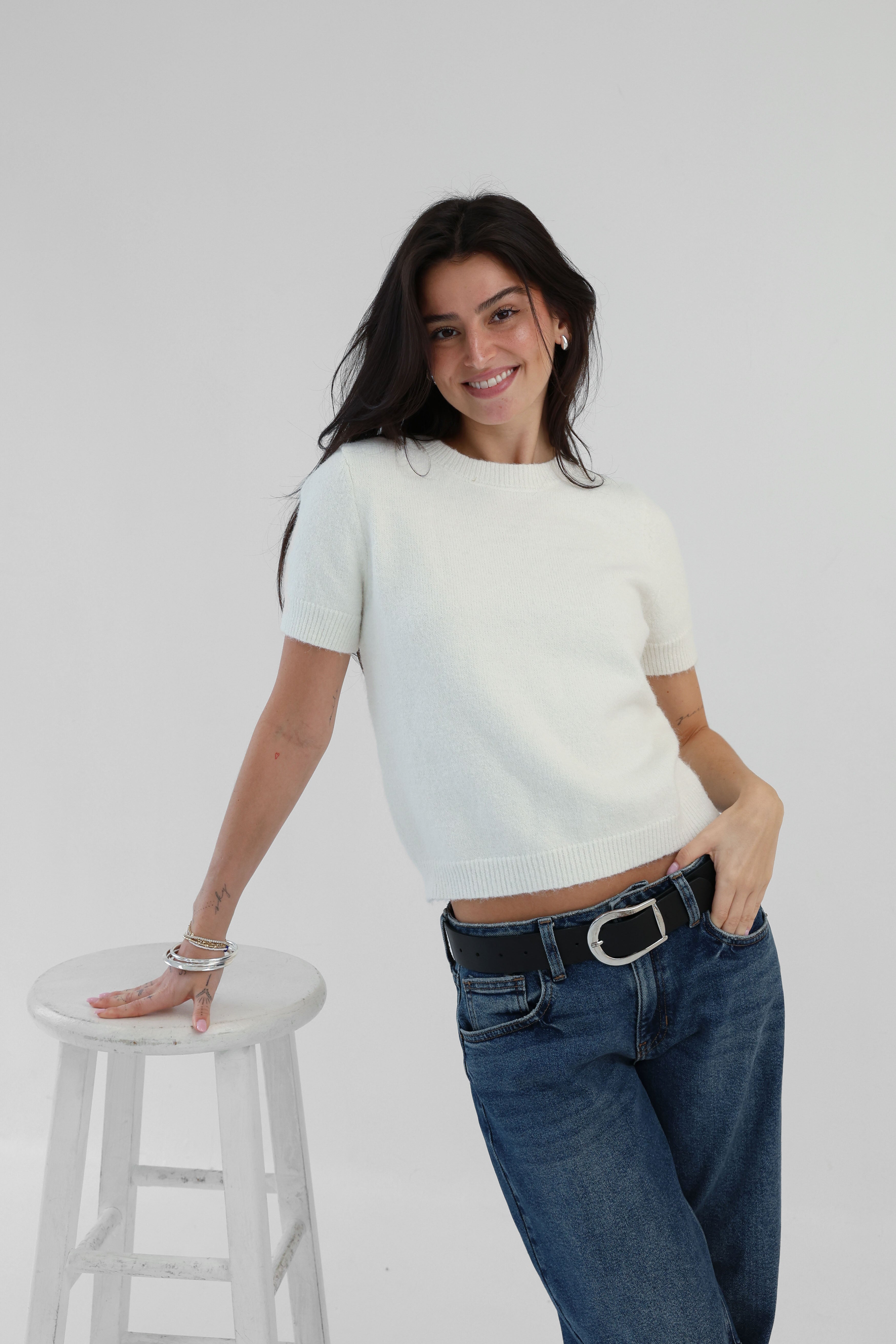 Woman wearing a white t-shirt and blue jeans standing on a white stool against a plain background