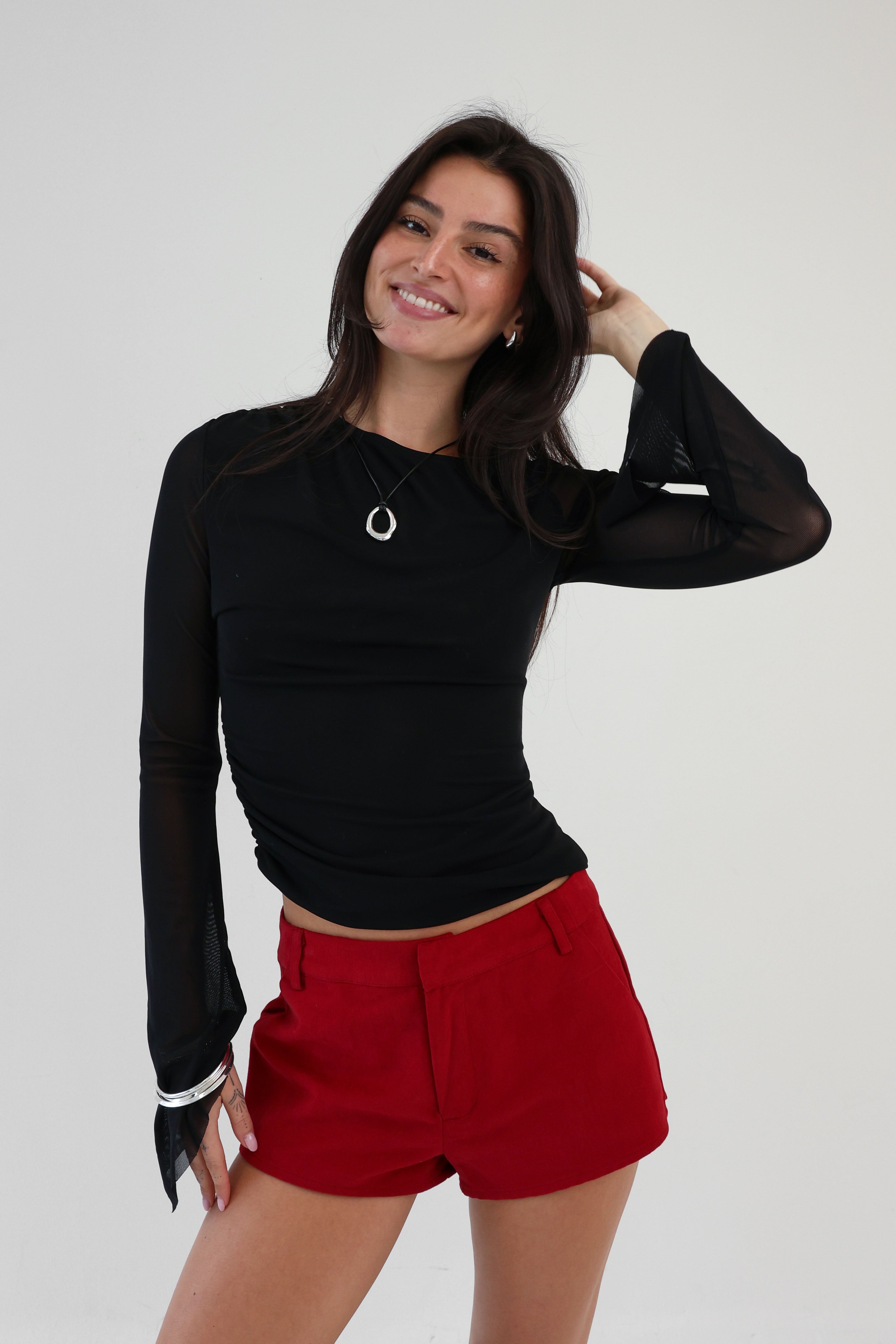 Woman wearing a black long-sleeve top and red shorts against a white background