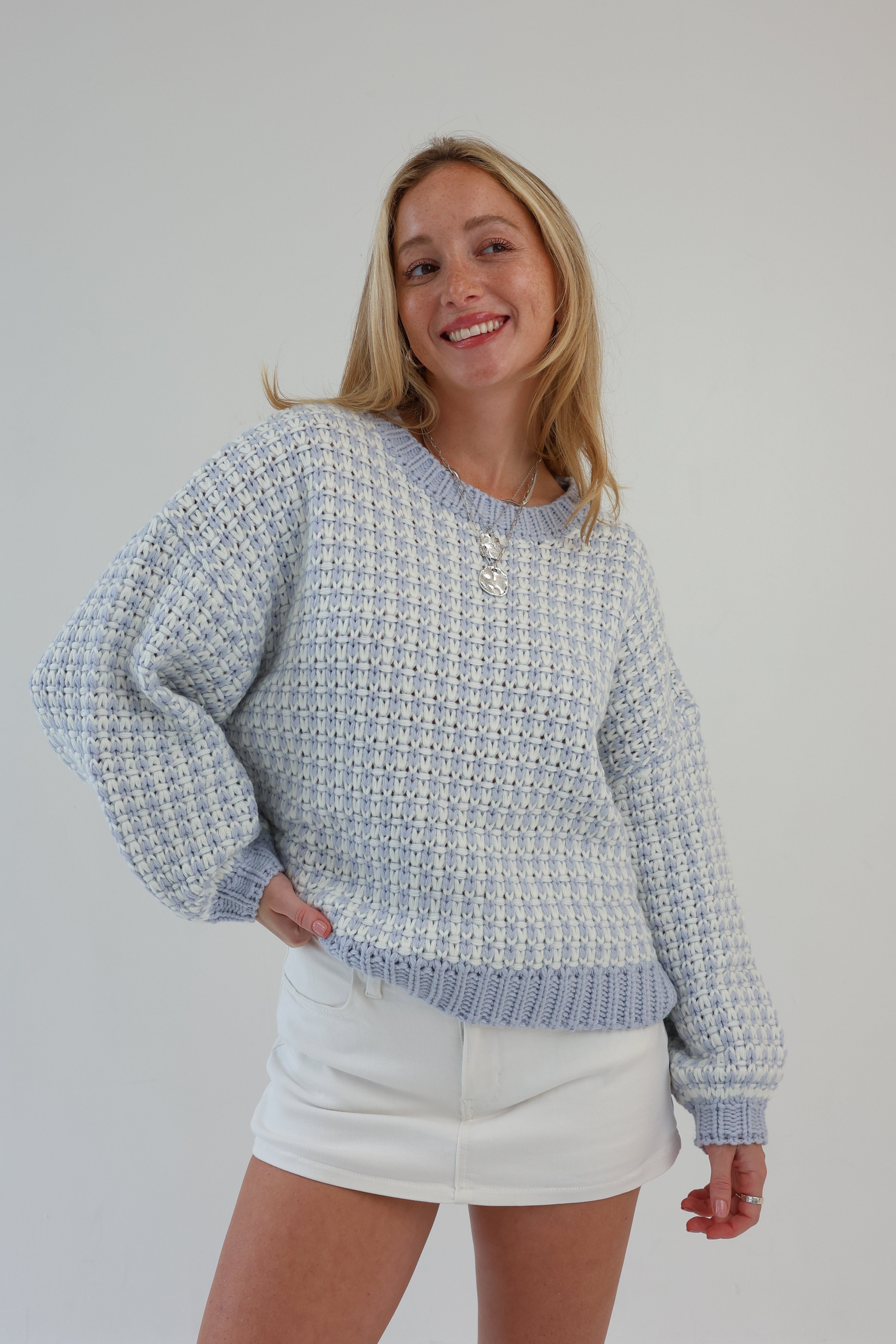 Woman wearing a patterned sweater and a white skirt against a plain background