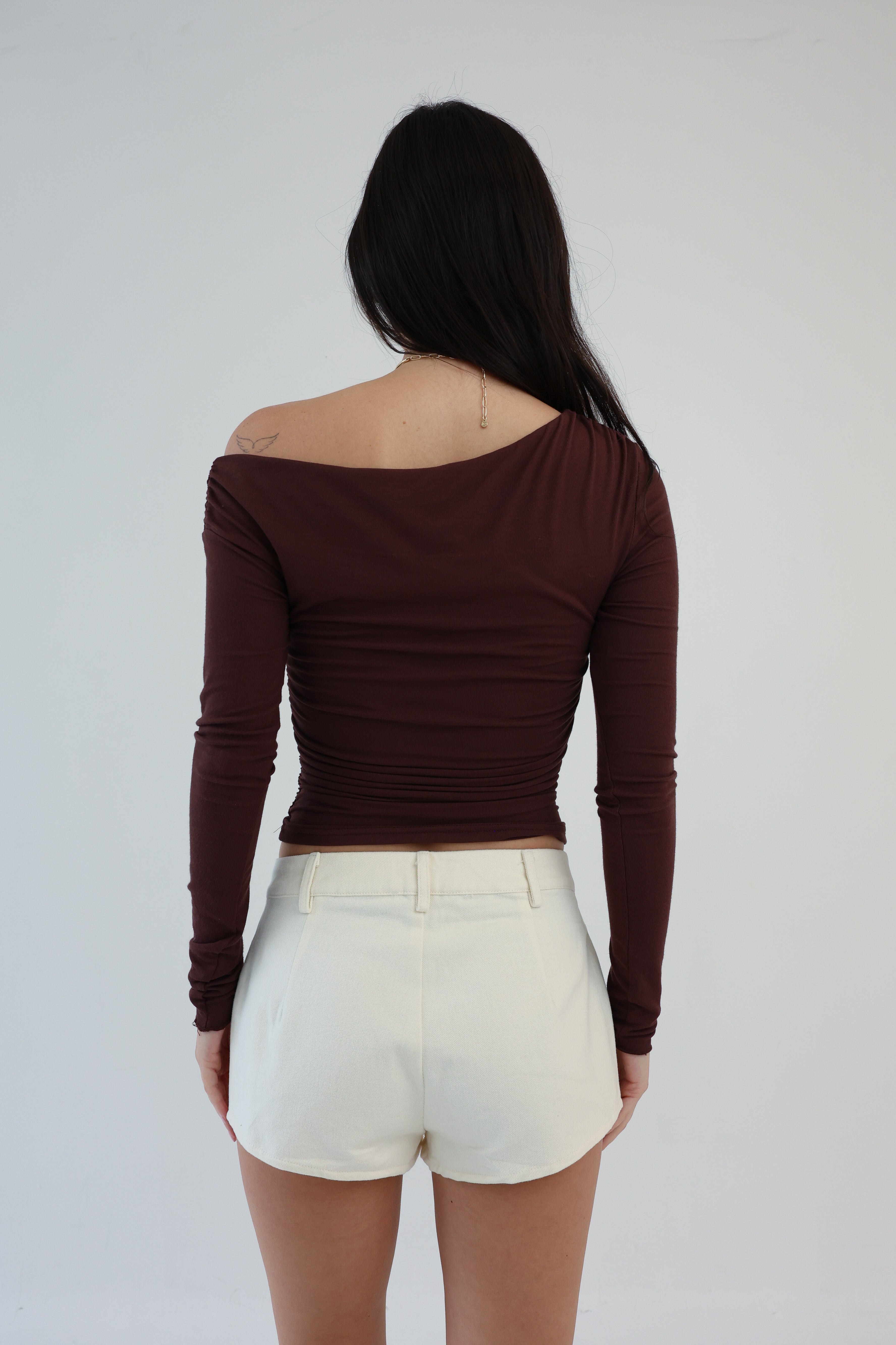 Person wearing a brown off-shoulder top and white shorts on a plain background