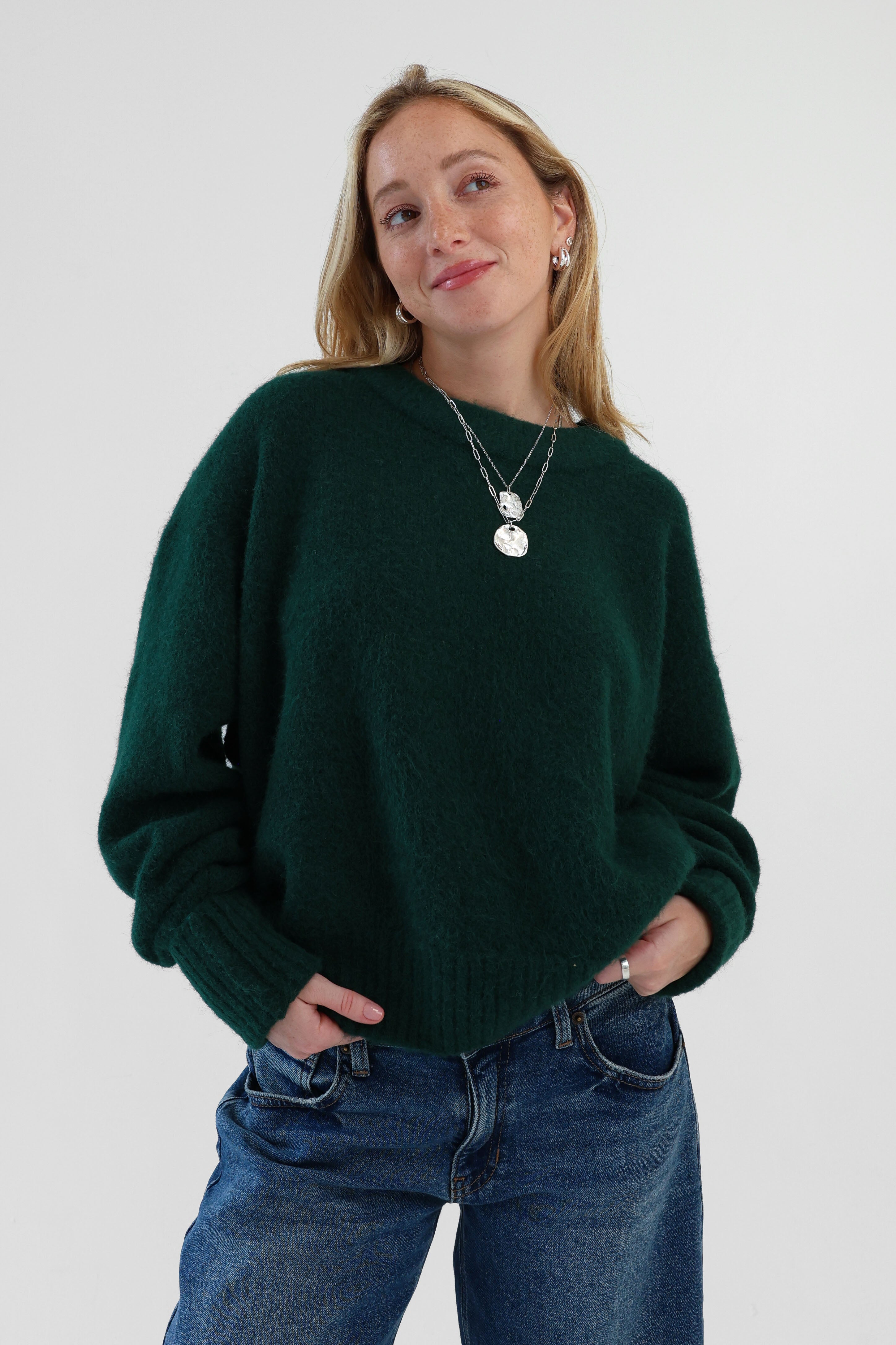 Woman wearing a dark green sweater and blue jeans against a white background