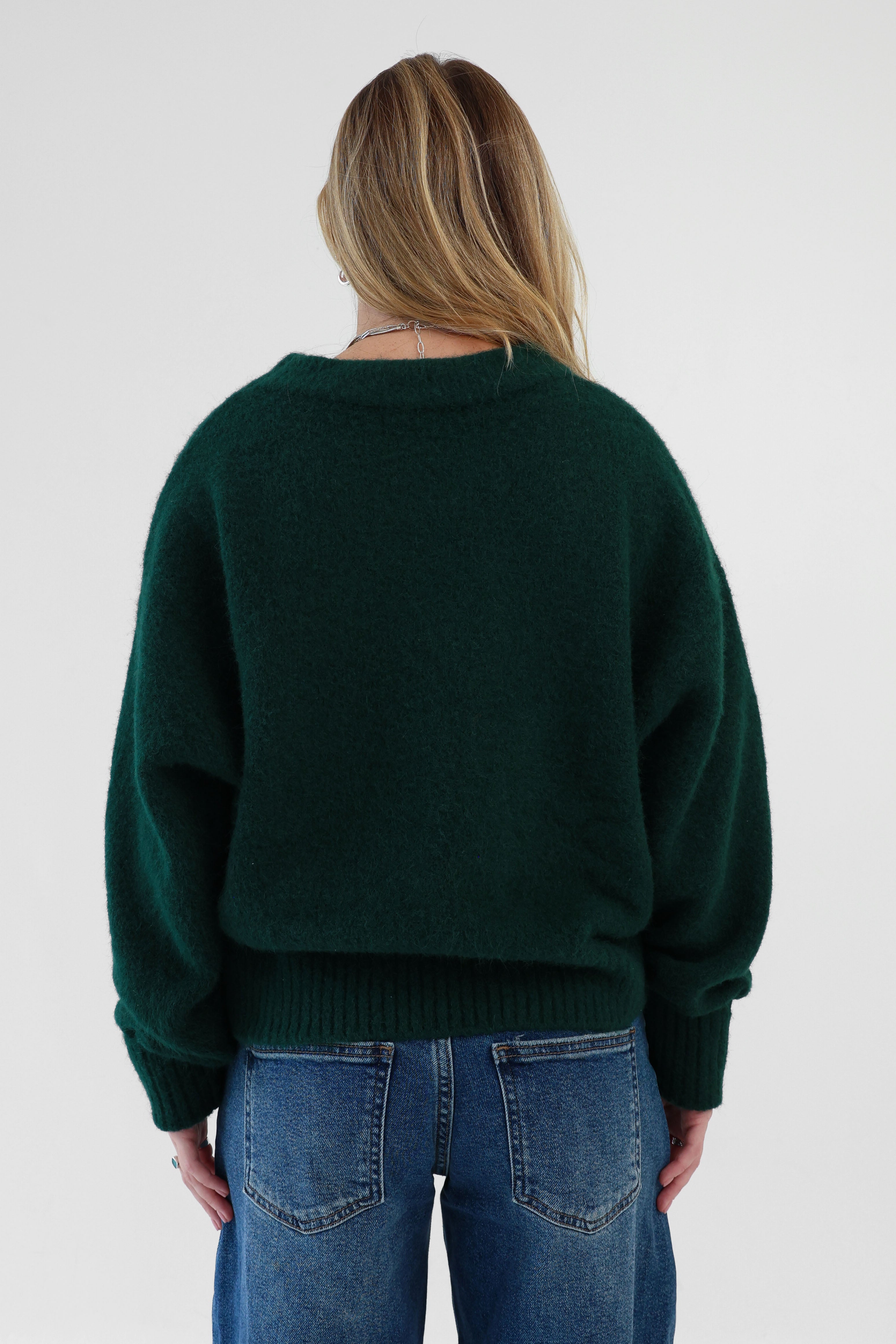 Person wearing a dark green sweater and blue jeans on a white background