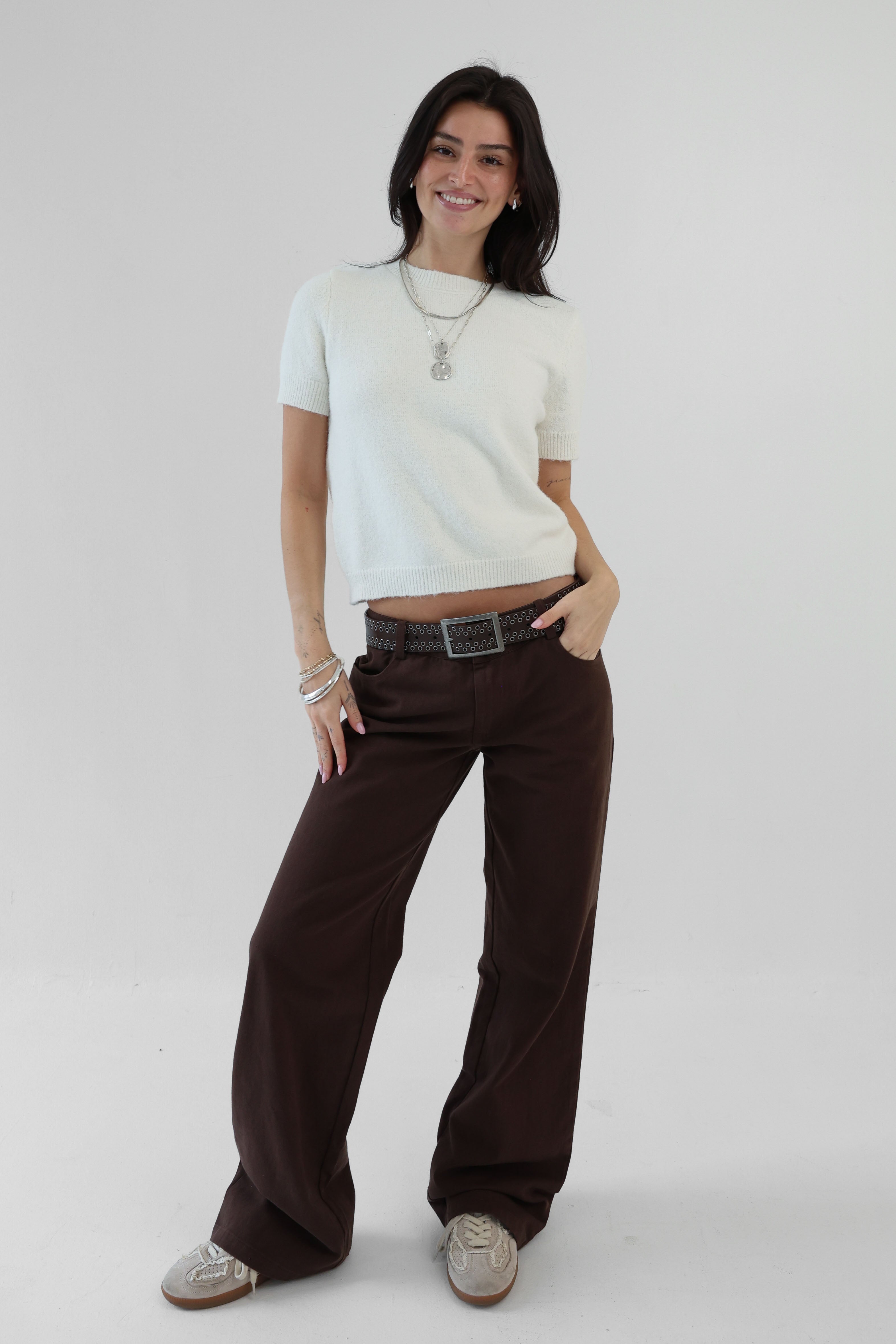 Woman wearing a white top and brown pants on a plain background