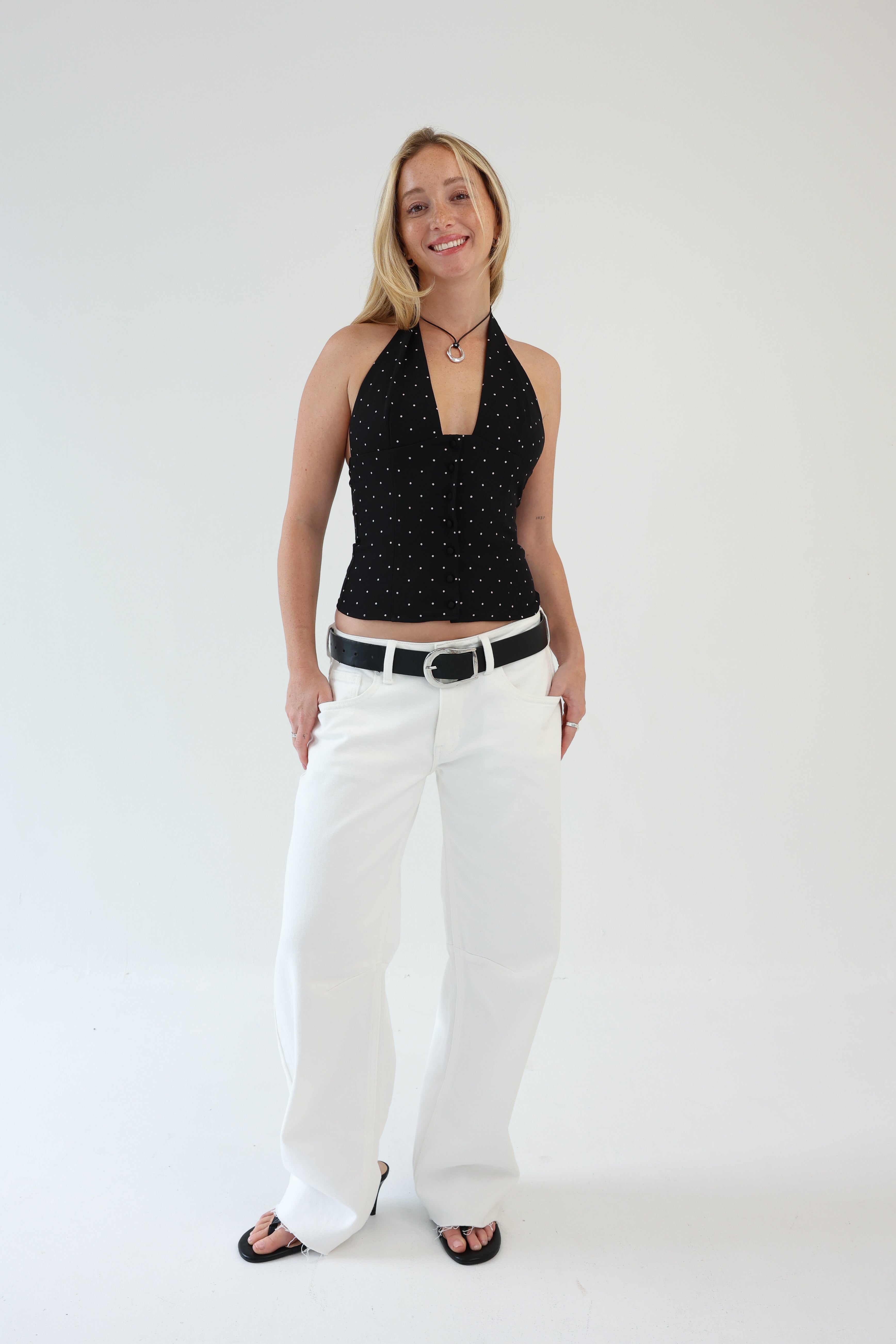 Woman wearing a black halter top with white polka dots and white pants on a plain background