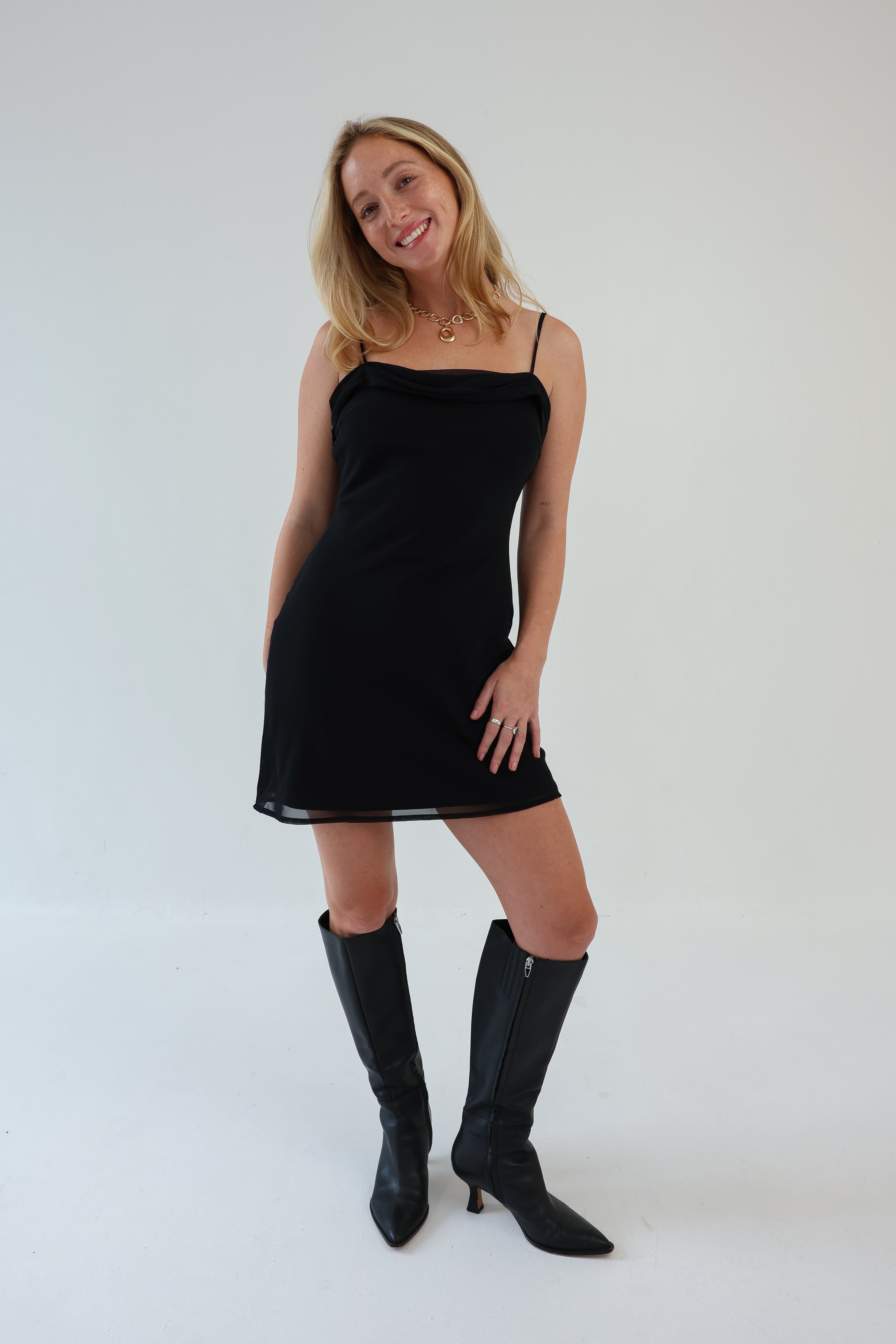 Woman wearing a black dress and black knee-high boots against a white background