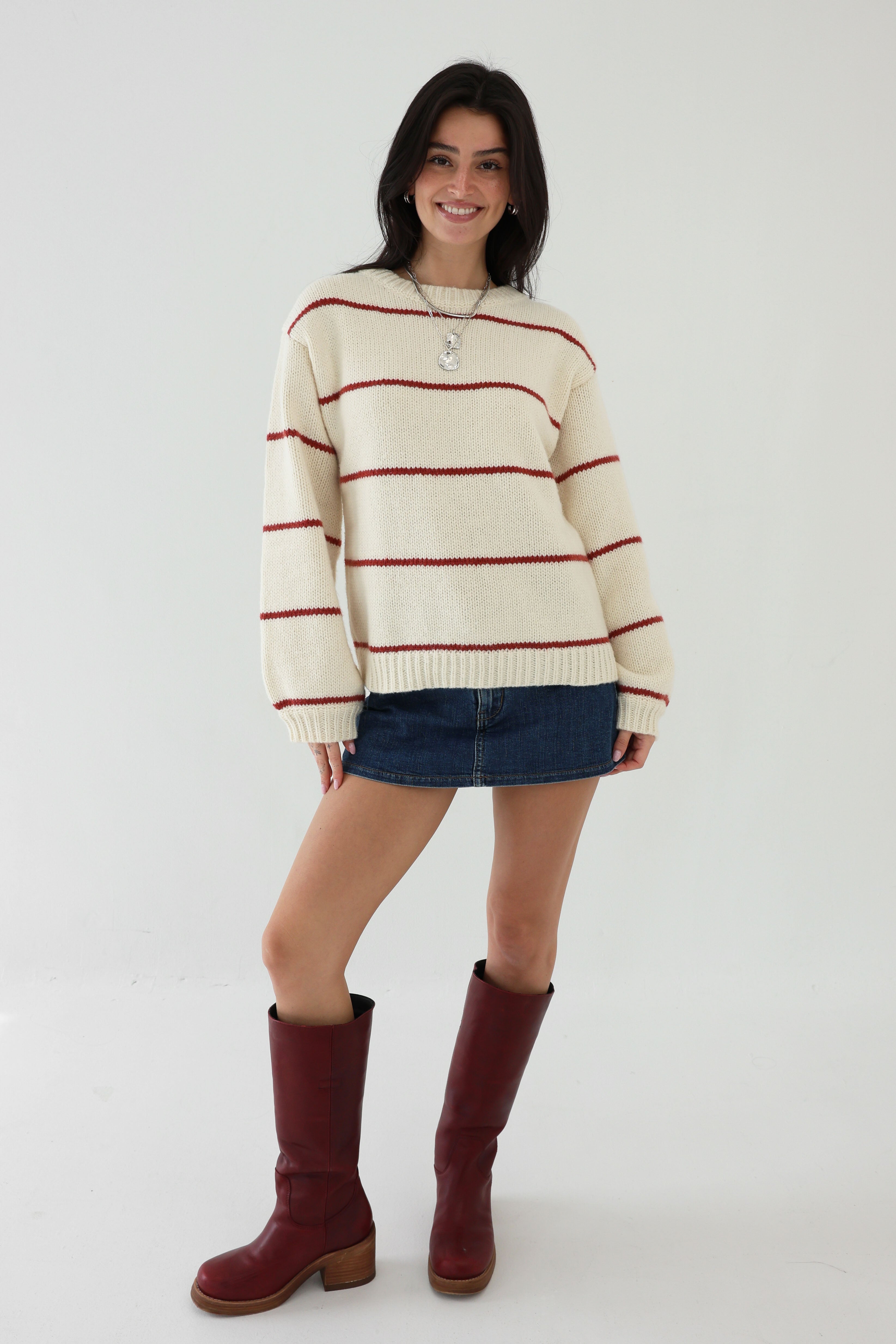 Woman wearing a striped sweater and skirt with red boots on a white background