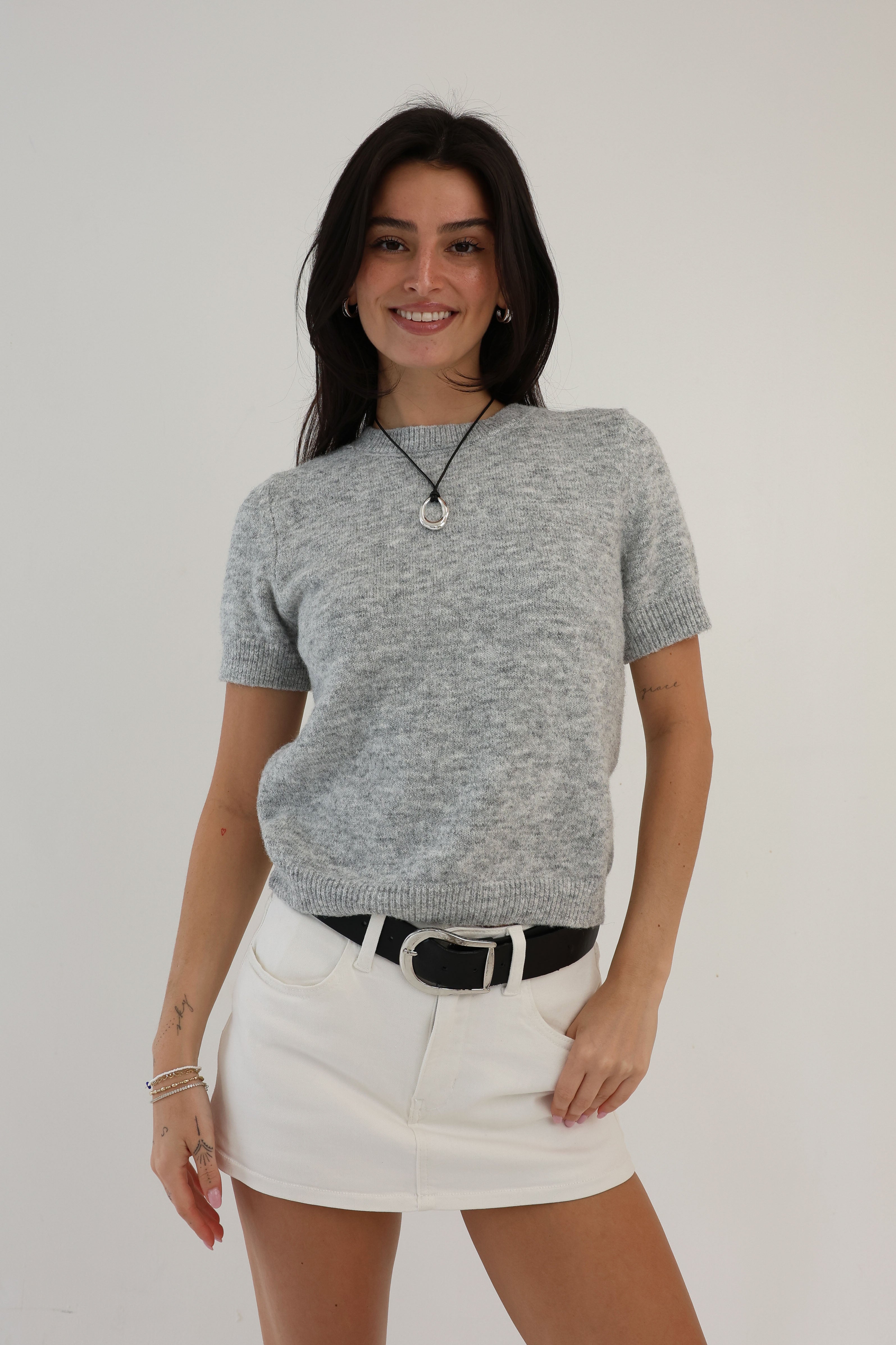Woman wearing a gray sweater and white skirt against a plain background