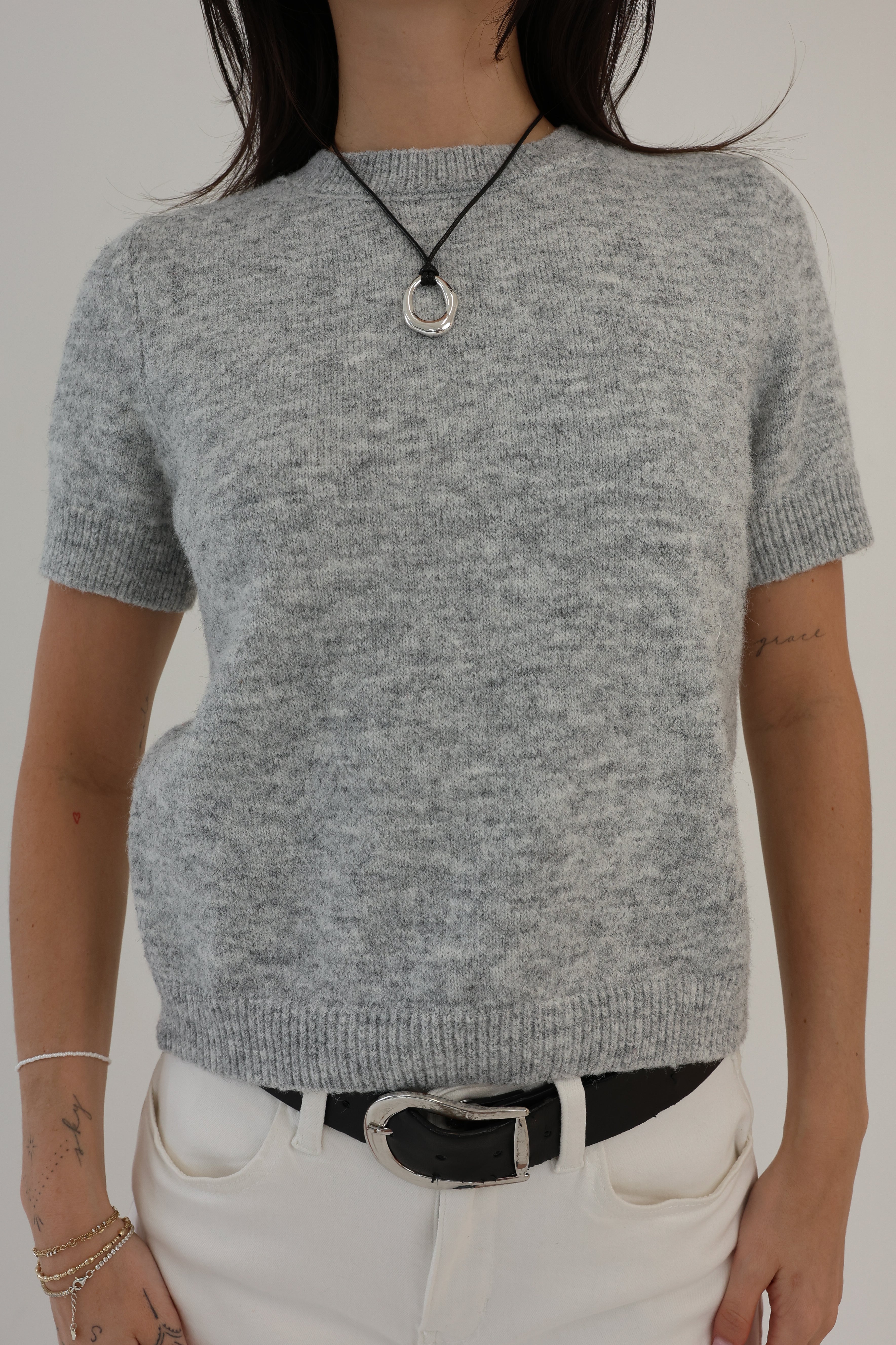 Person wearing a gray sweater and white pants against a plain background