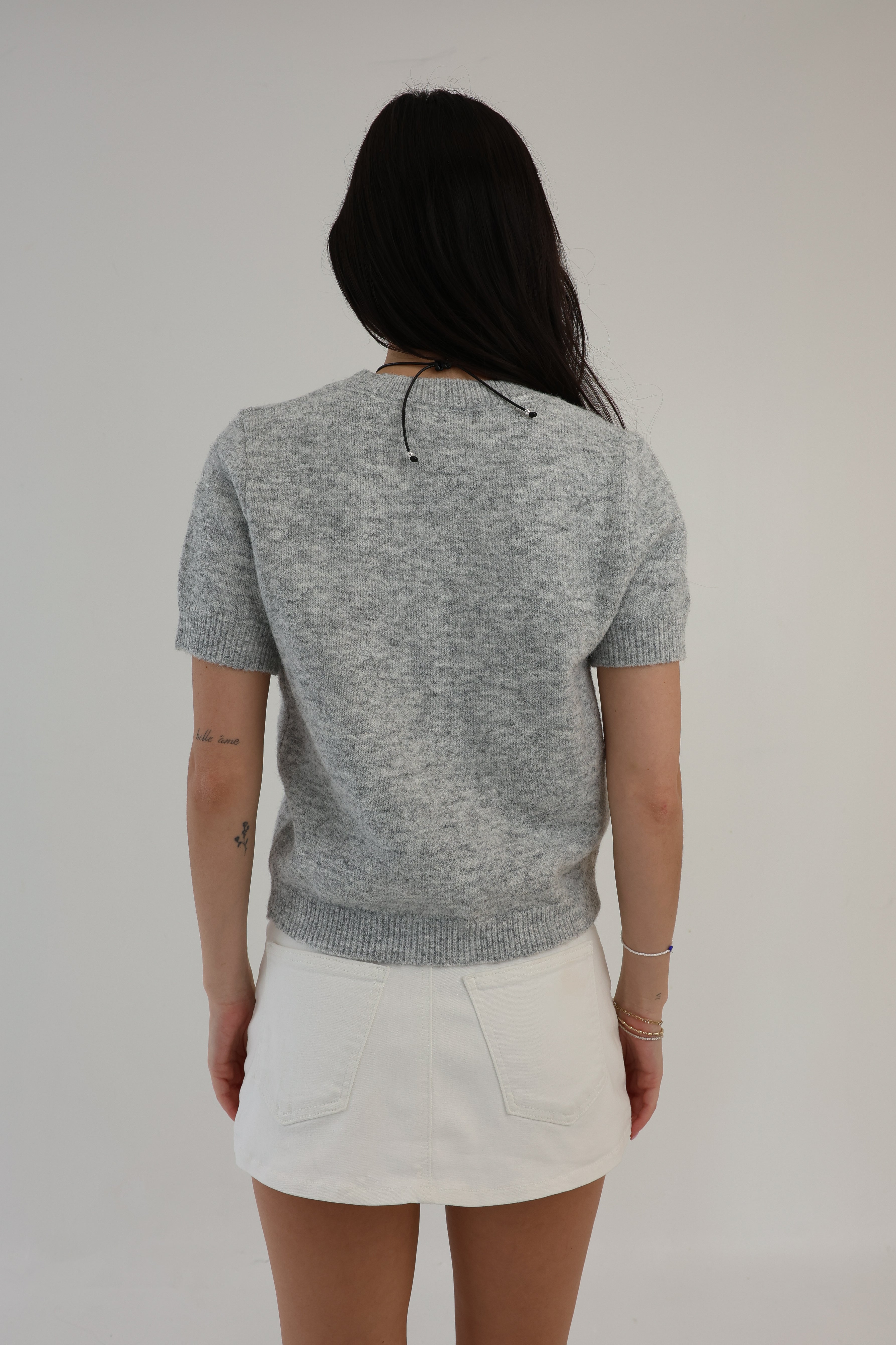 Person wearing a gray knit top and white skirt on a plain background