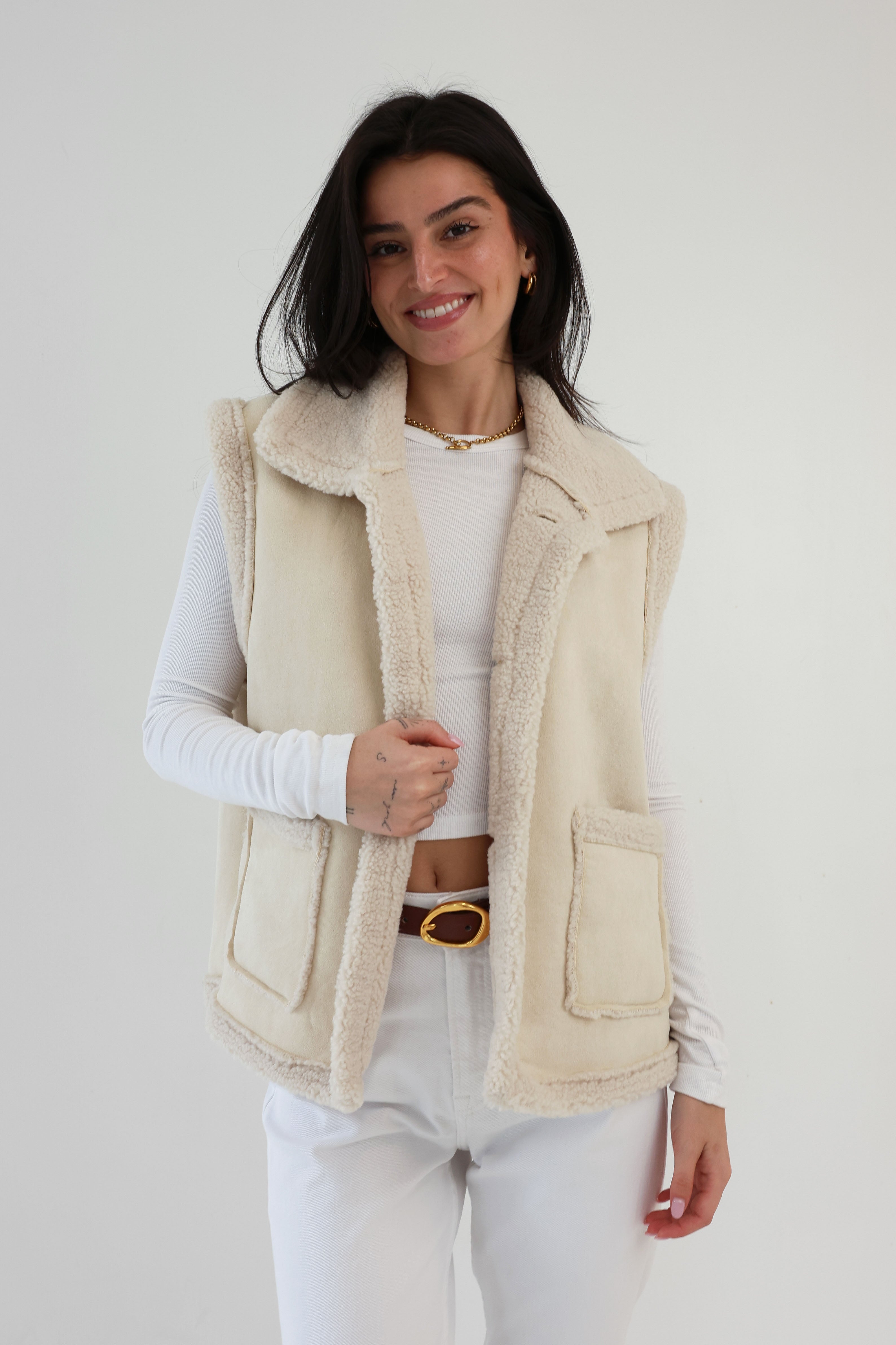 Woman wearing a beige vest over a white outfit against a plain background