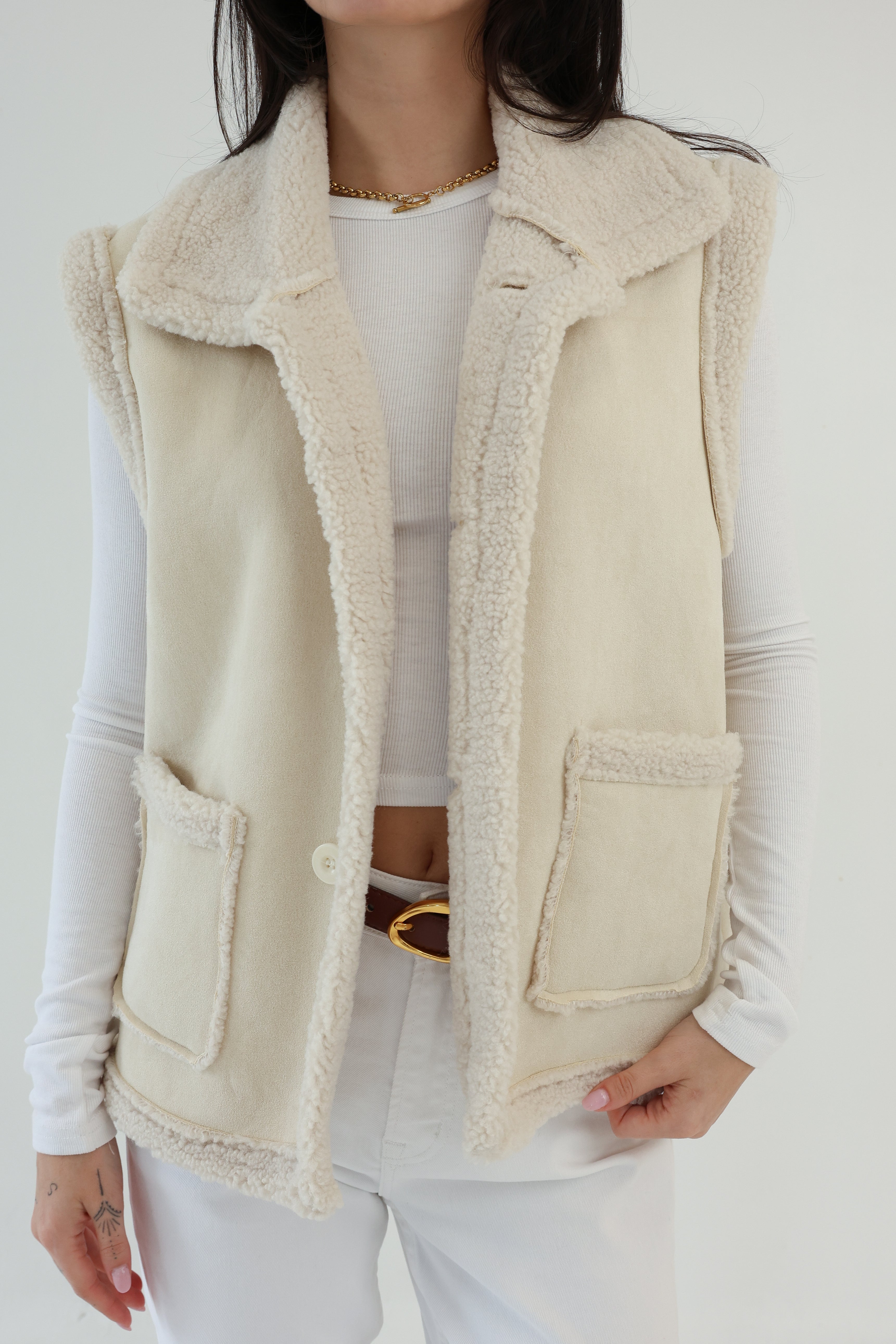 Person wearing a beige fleece vest over a white outfit against a plain background