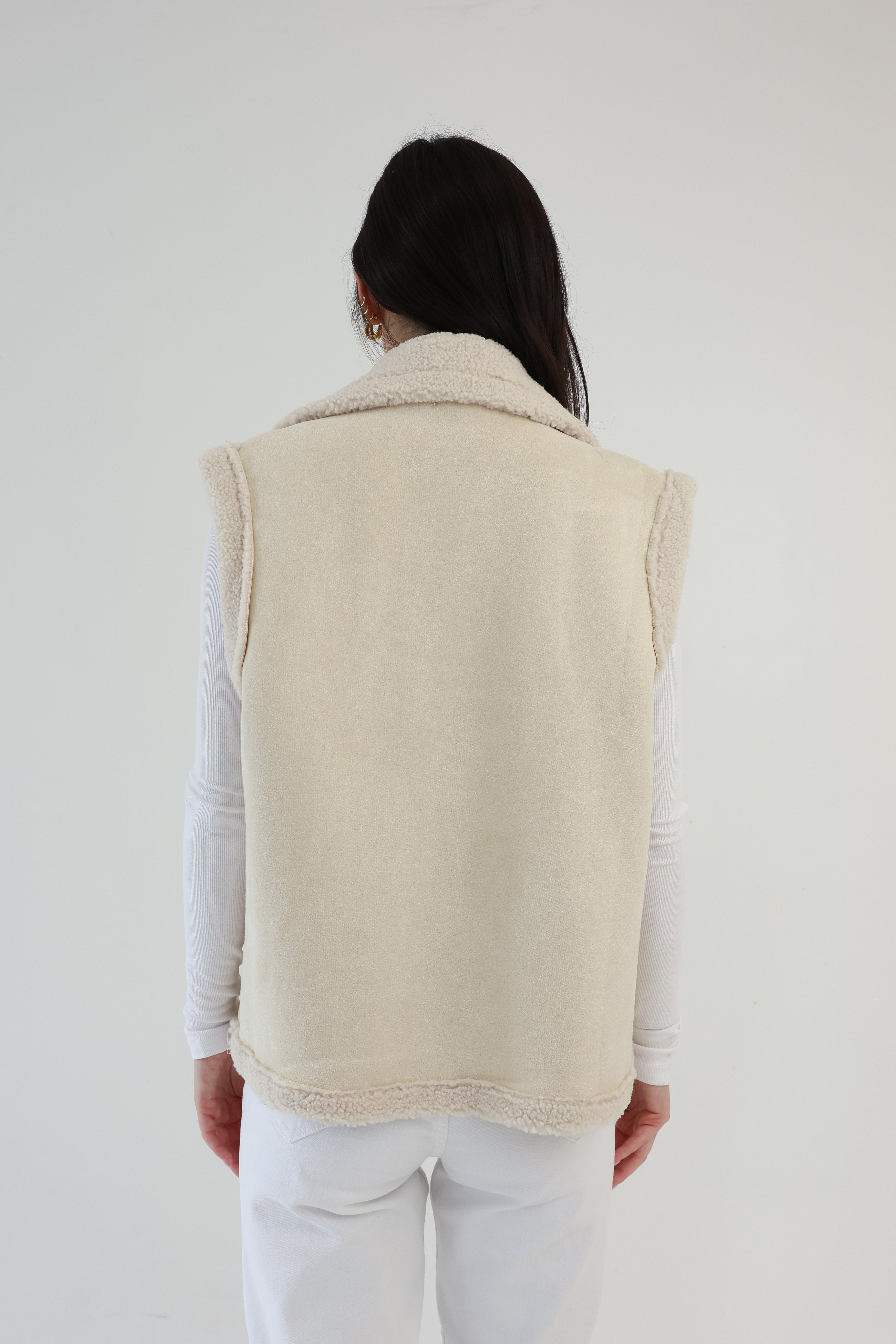 Person wearing a beige vest over a white shirt and pants on a plain background