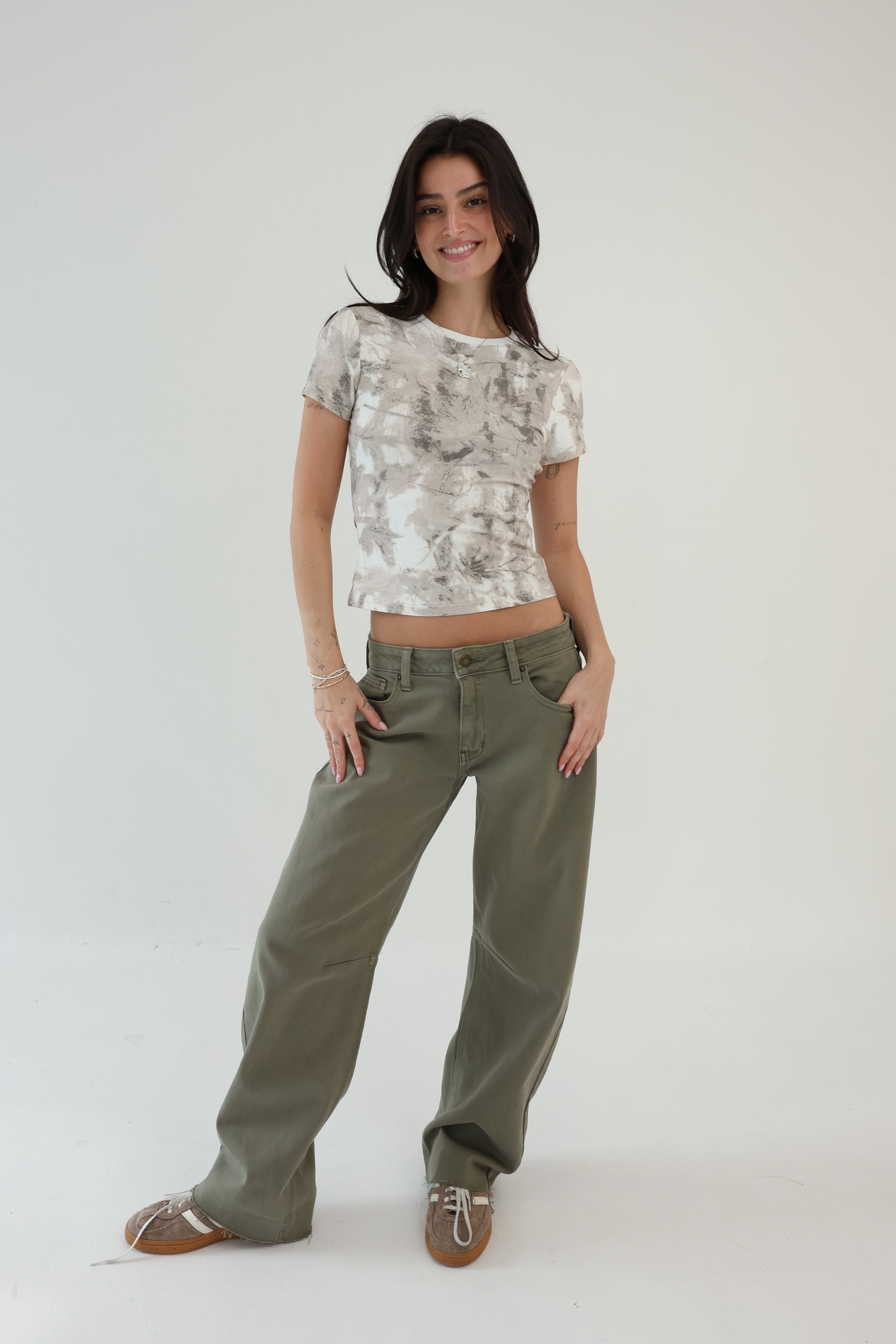 Woman wearing a patterned top and green pants on a white background