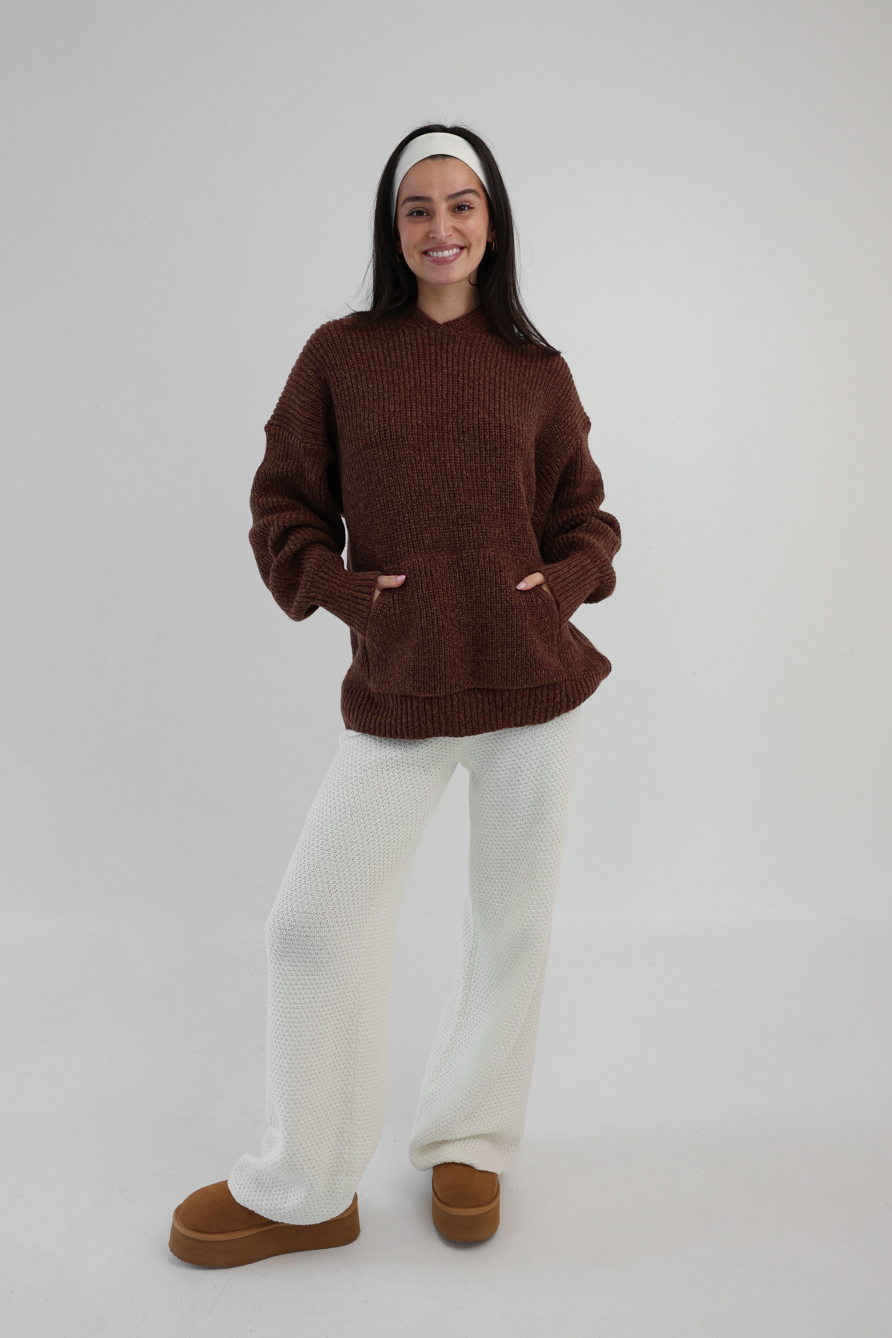 Person wearing a brown sweater, white pants, and brown shoes on a white background