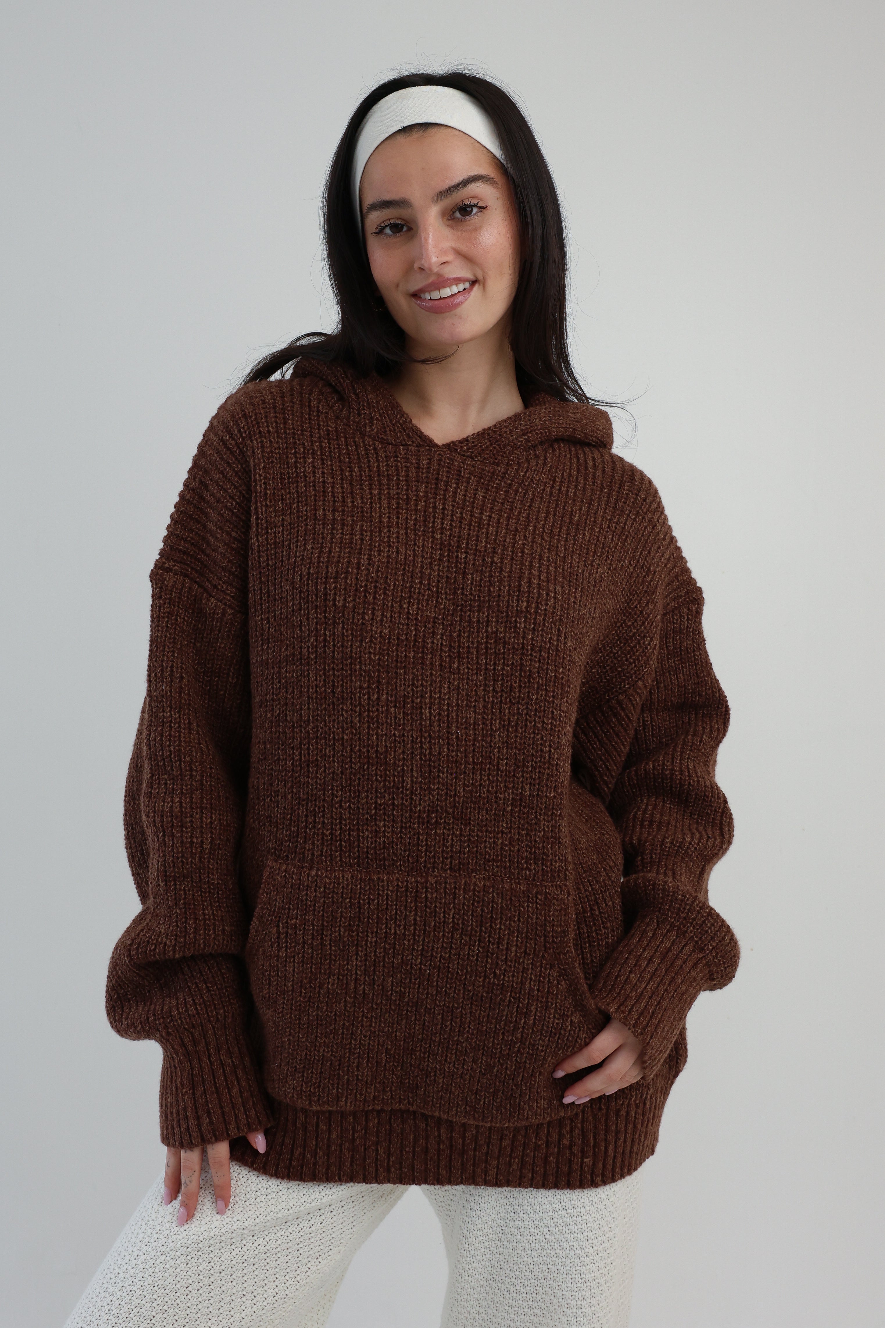 Woman wearing a brown sweater with a hood on a plain background