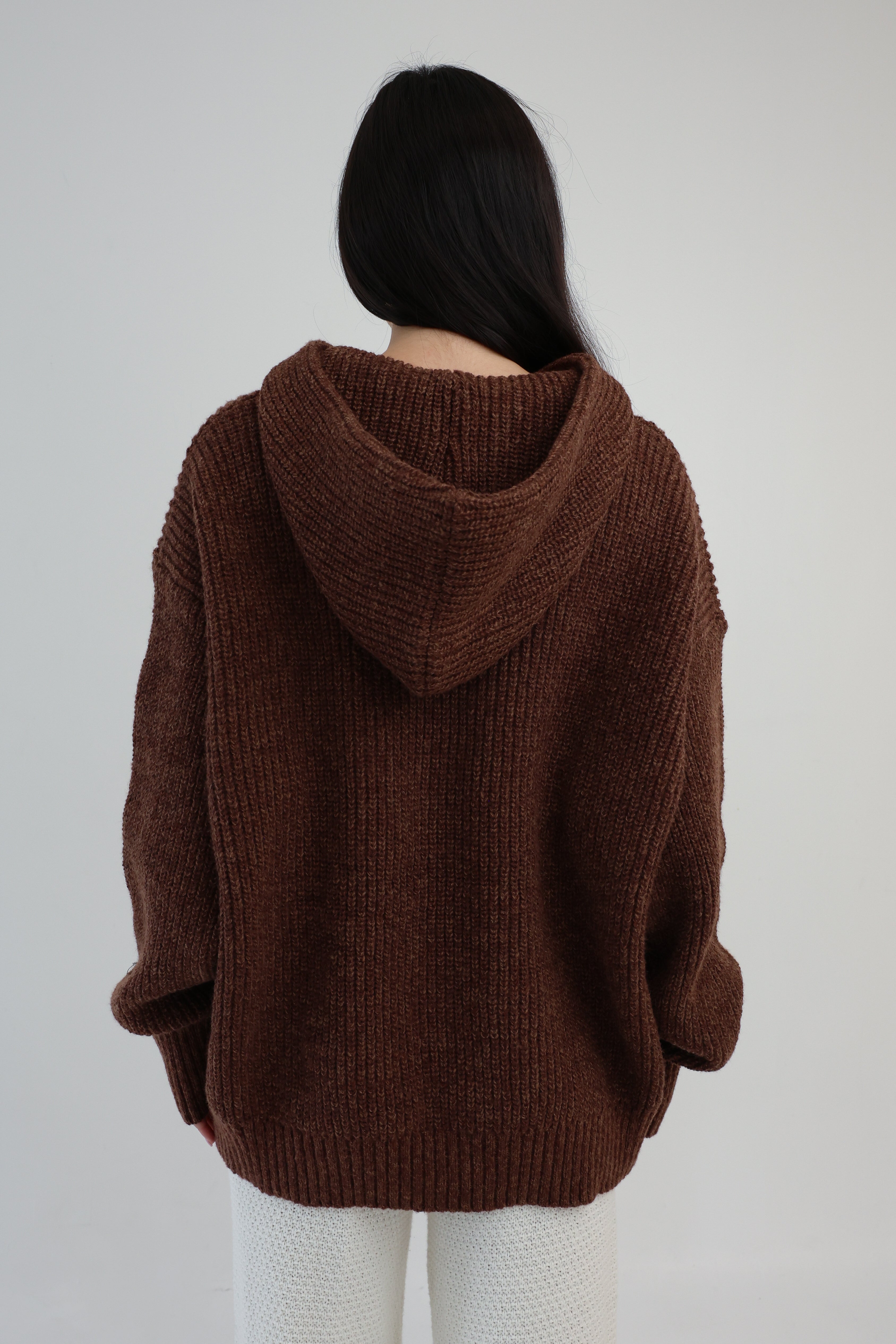 Person wearing a brown knitted hoodie against a plain background