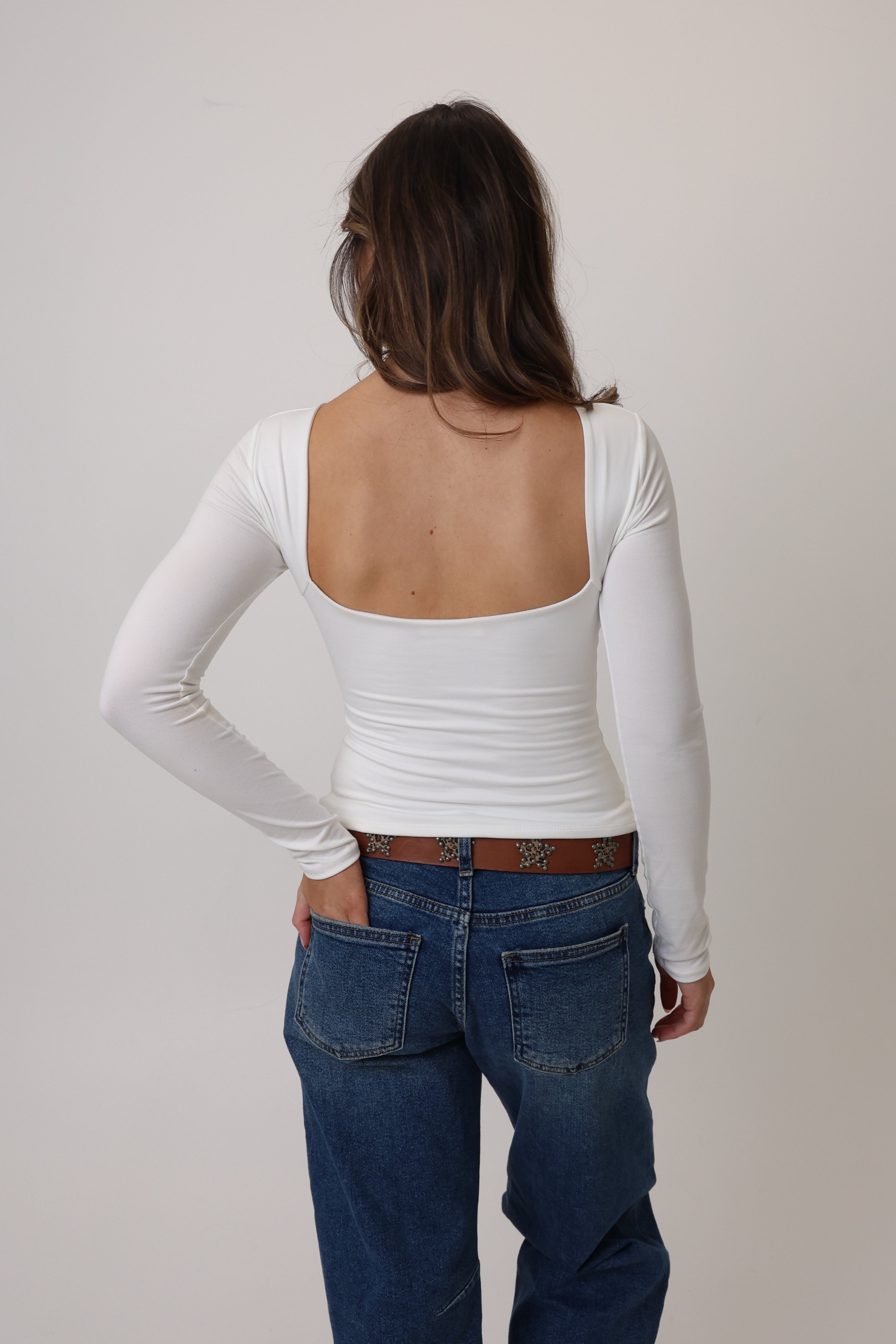Person wearing a white long-sleeve top and blue jeans on a plain background