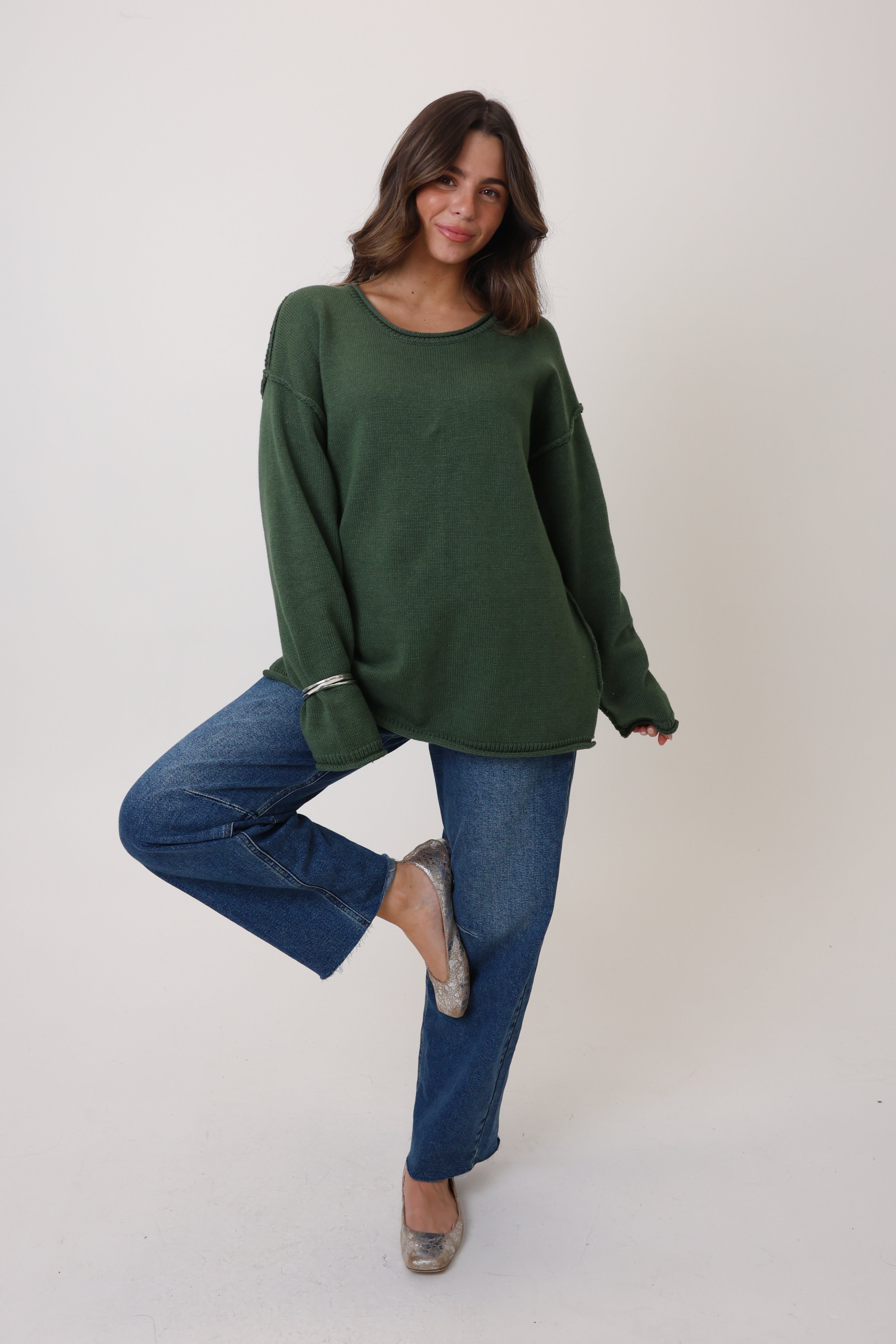 Woman wearing a green sweater and blue jeans on a white background