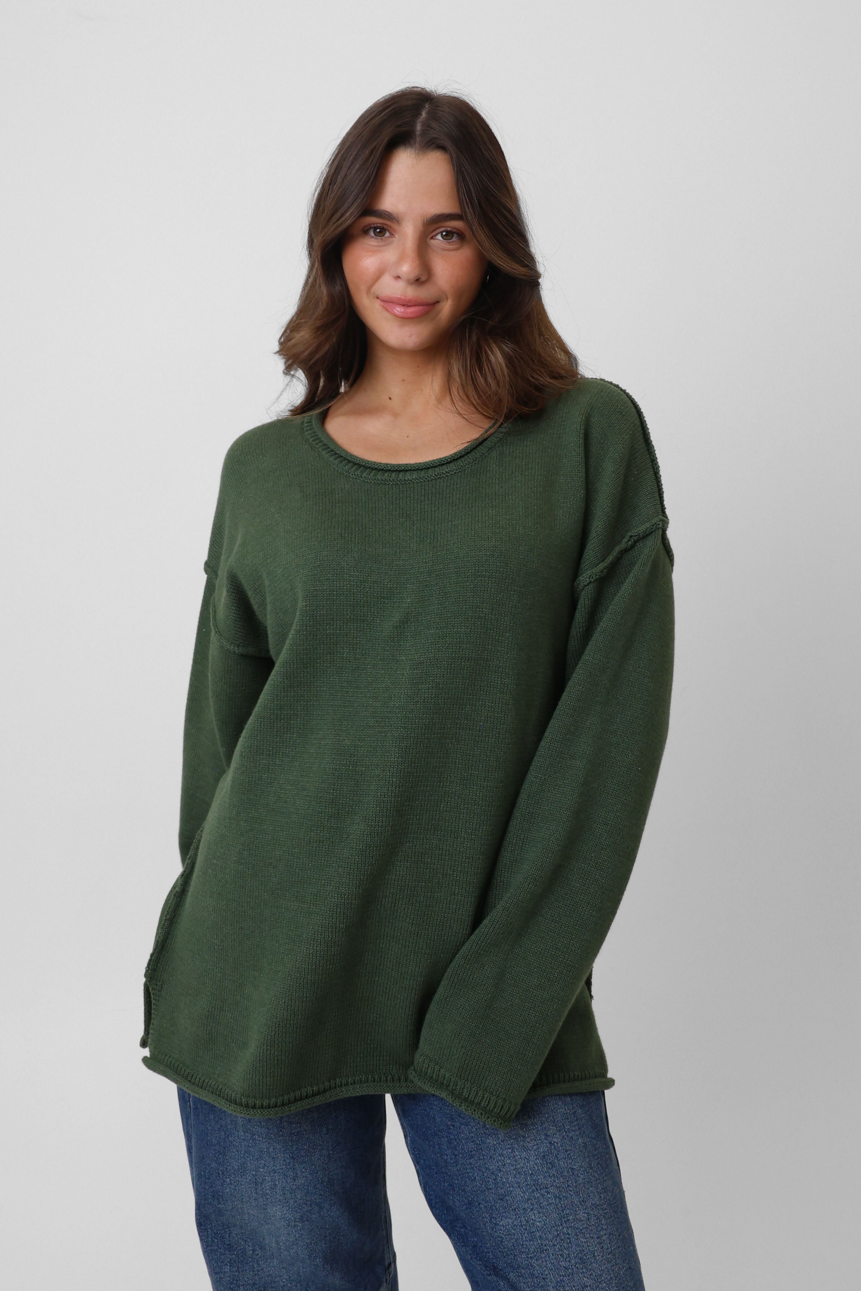 Woman wearing a green sweater and blue jeans on a white background
