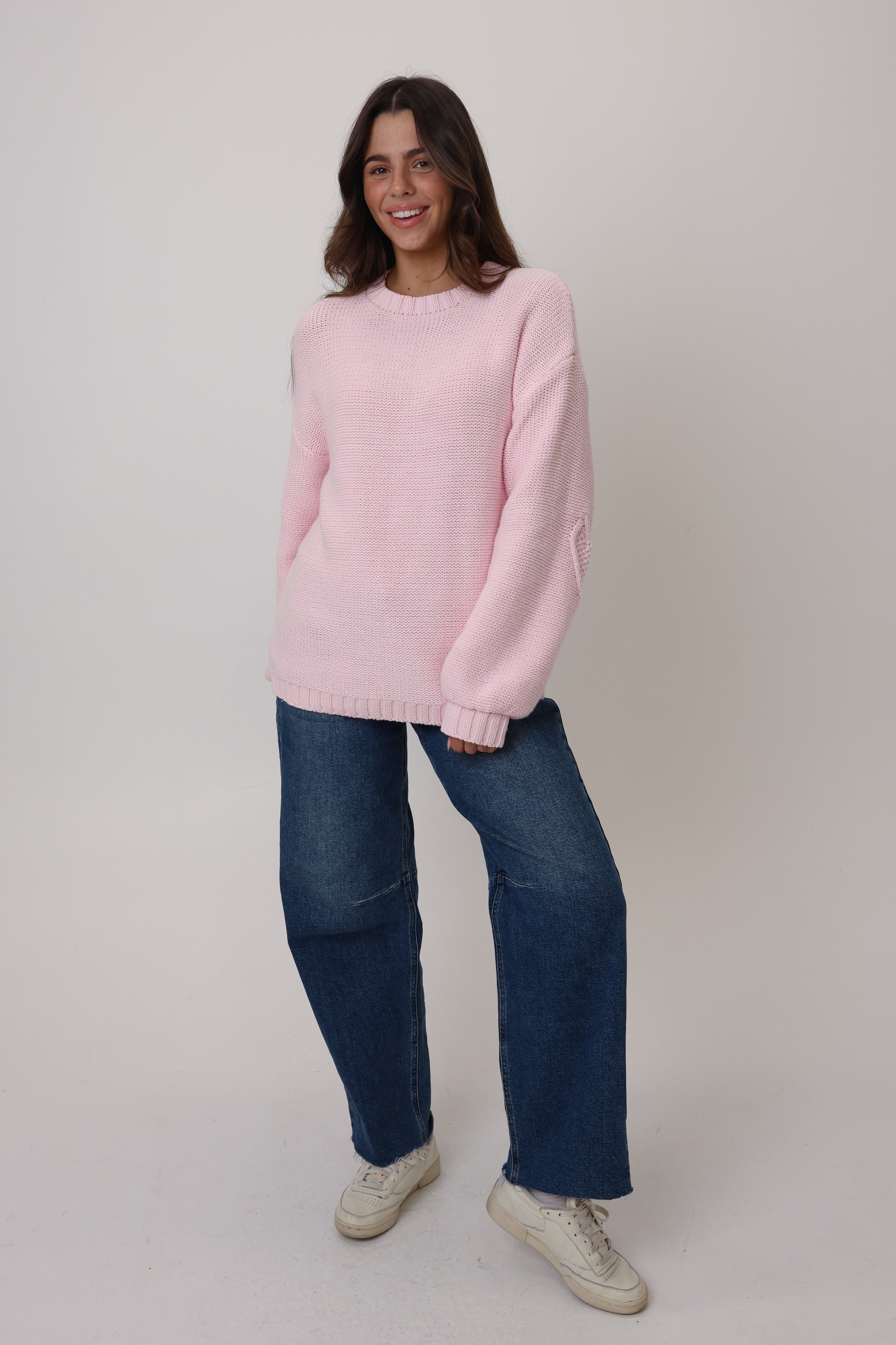 Woman wearing a pink sweater and blue jeans on a white background