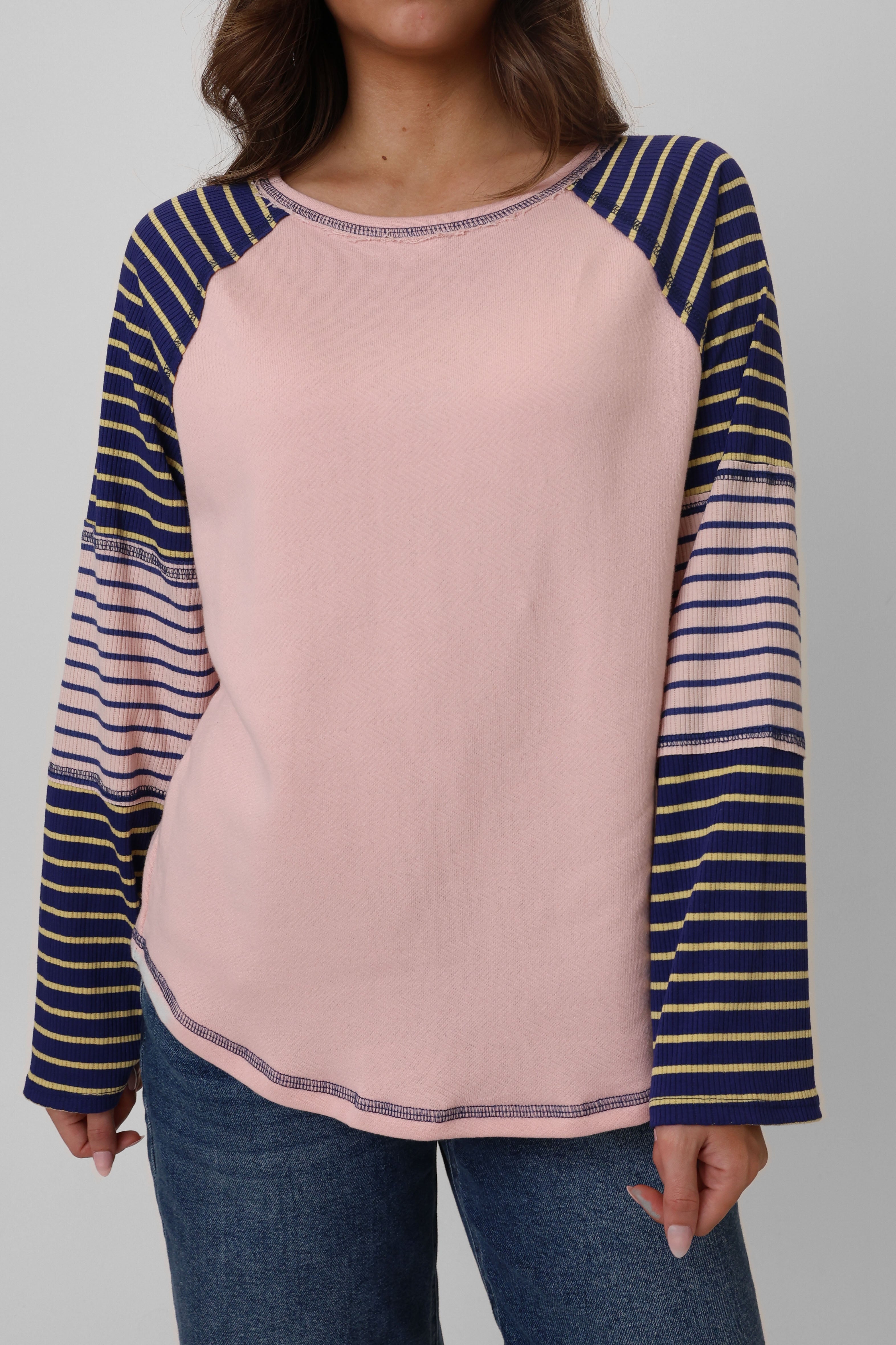 Pink long-sleeve top with blue and yellow striped sleeves worn by a person on a gray background