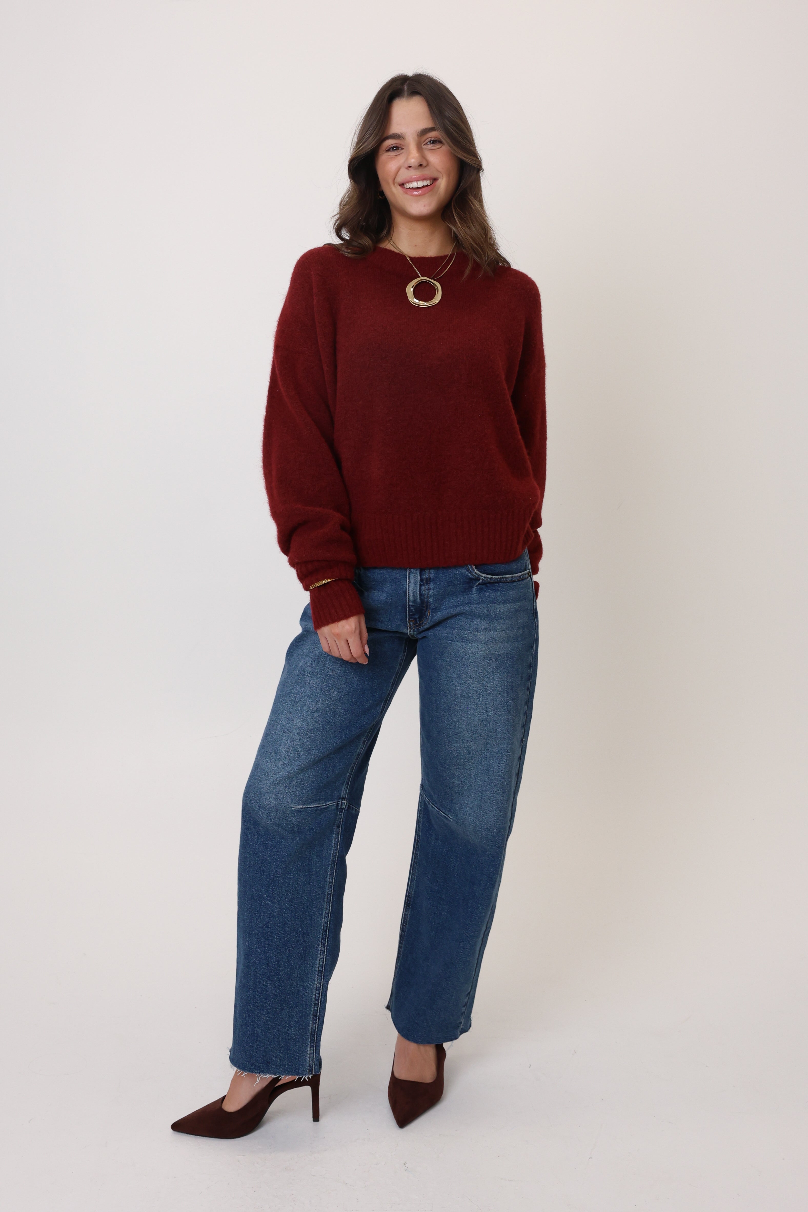 Woman wearing a burgundy sweater and blue jeans on a white background